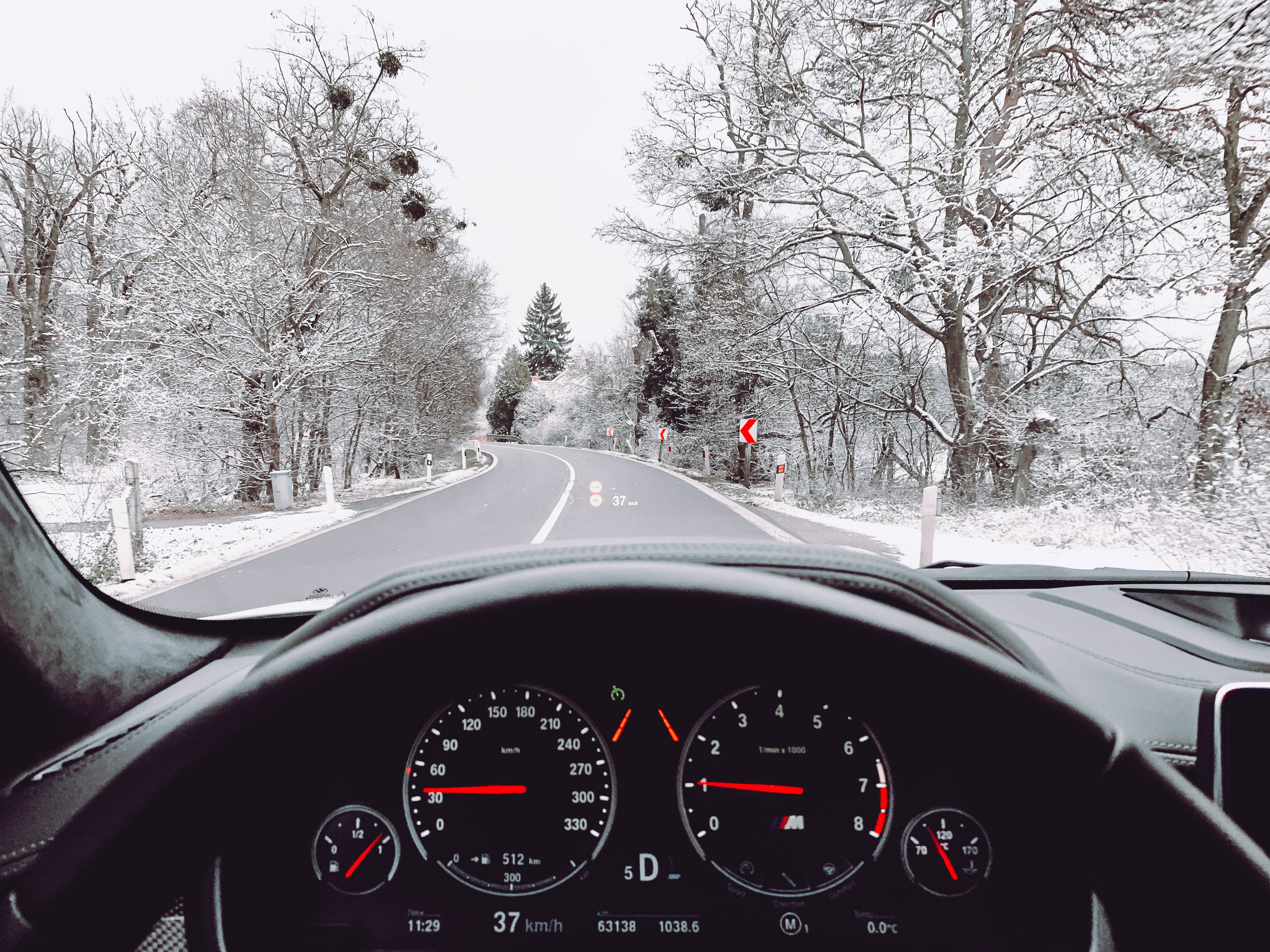 冬季桌面 桌布 壁紙 — 穿過白雪覆蓋的森林道路，兩旁是光禿禿的樹木，前方是蜿蜒的柏油路。