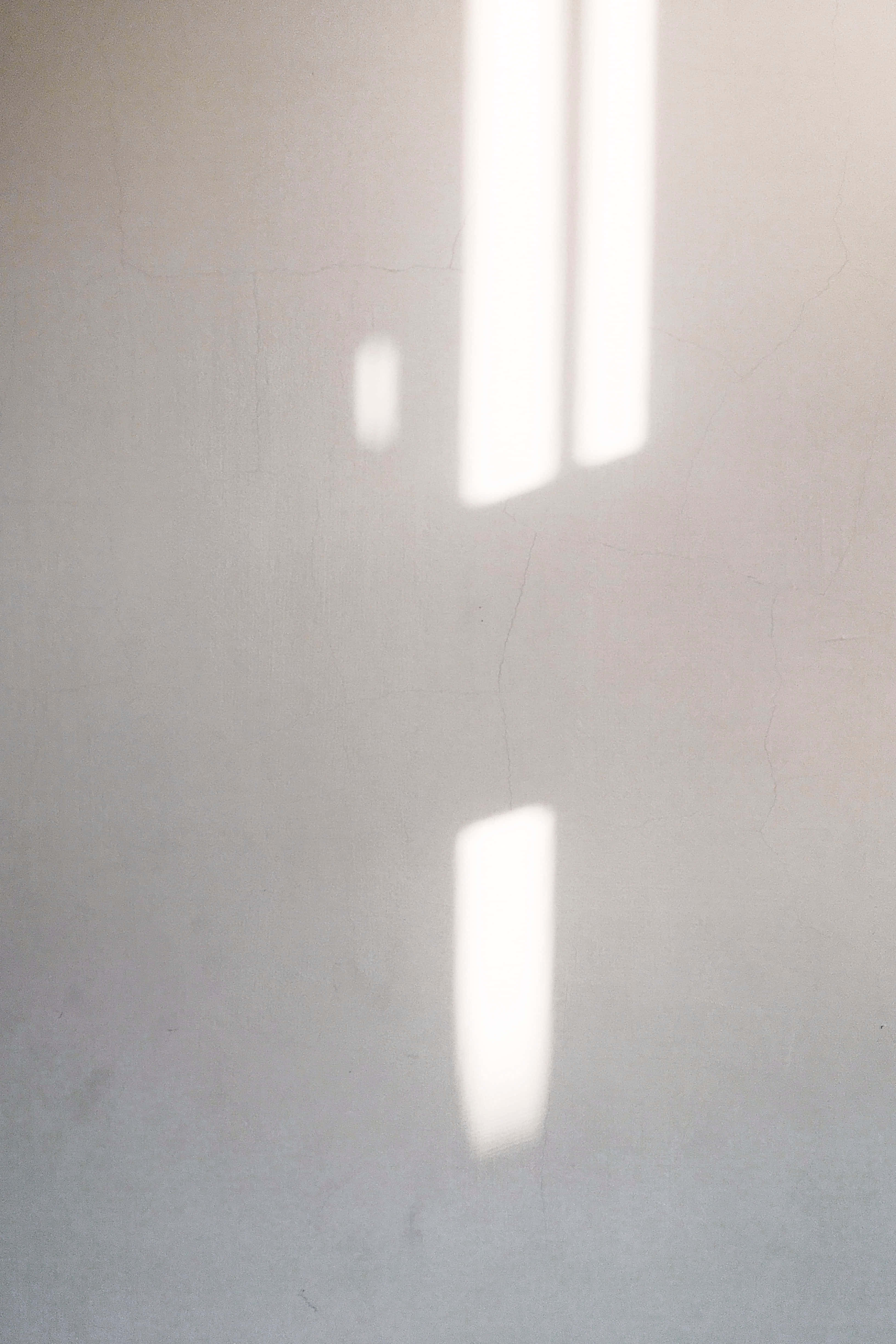 Sunlight 桌布 壁紙 — 窗簾投射出的柔和矩形光線，照在有細微裂紋的紋理米白色牆壁上。