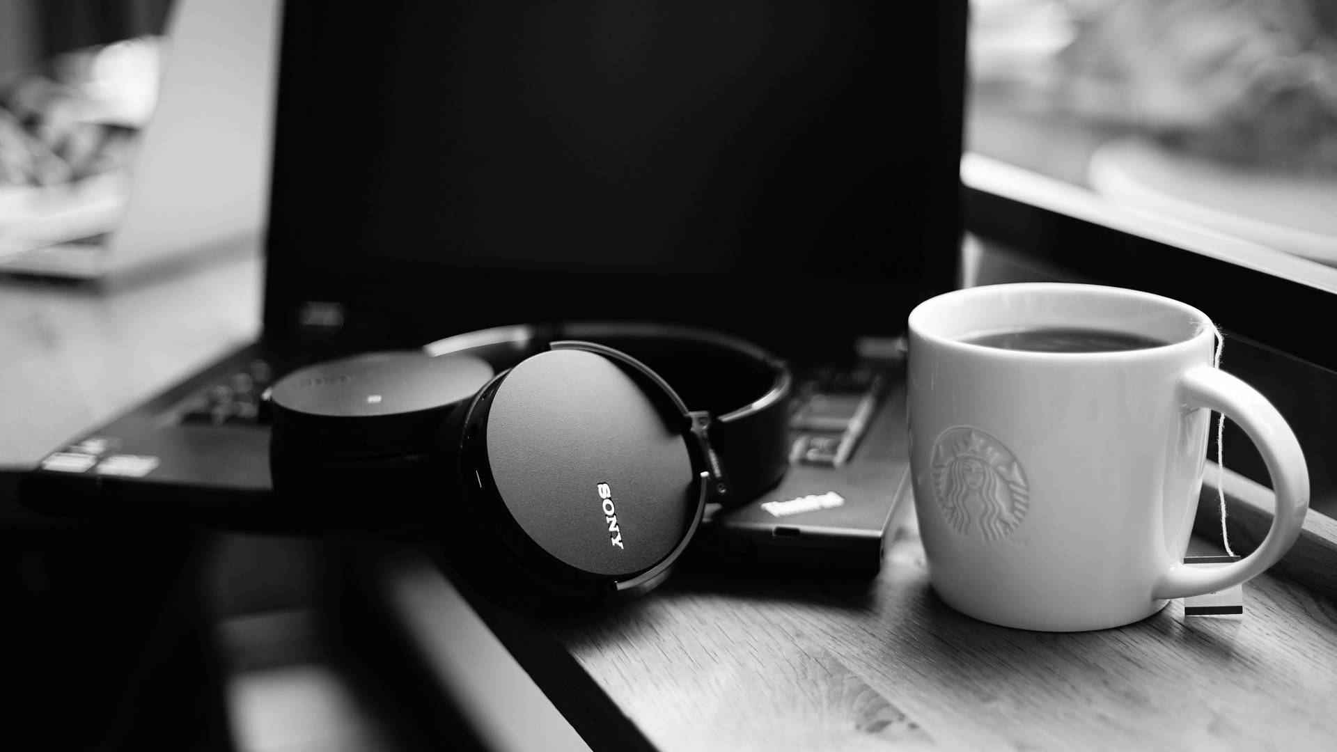 星巴克 桌布 壁紙 — 窗邊木桌上Sony耳機、筆記型電腦和Starbucks咖啡杯的黑白靜物照。