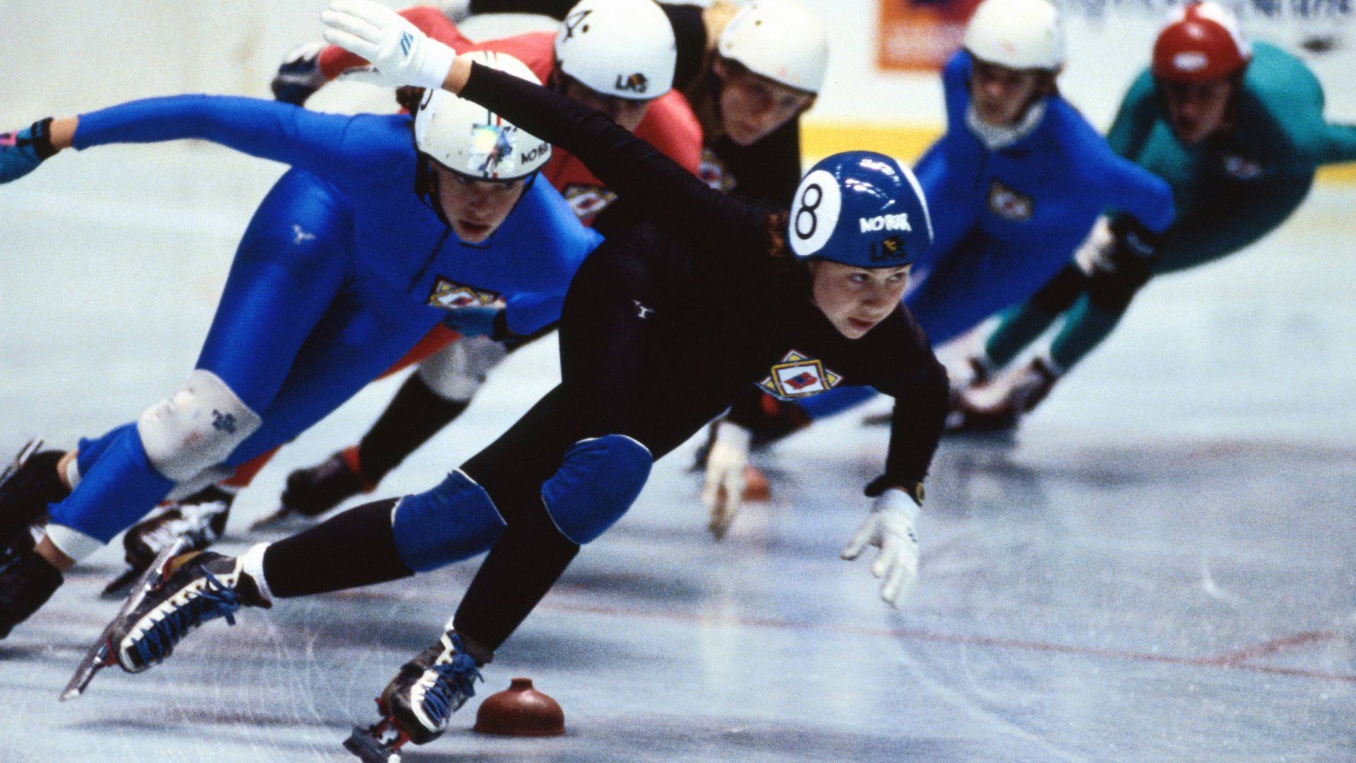 Speed 桌布 壁紙 — 競技性短道競速滑冰選手在冰場上以強烈的專注力和動態動作傾斜入彎。