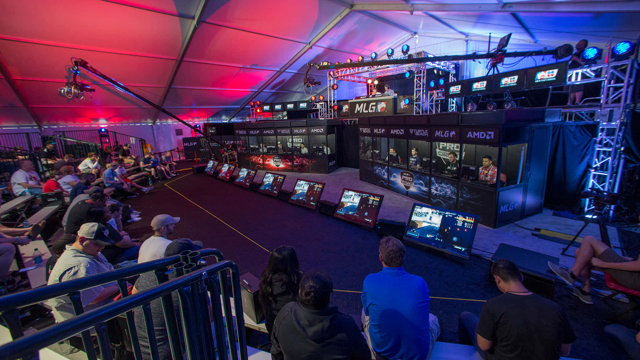 Gaming Tournaments 桌布 壁紙 — 競技玩家在充滿活力的電競場館中，在紅色和藍色舞台燈光下激烈對戰，觀眾們專注地觀看。