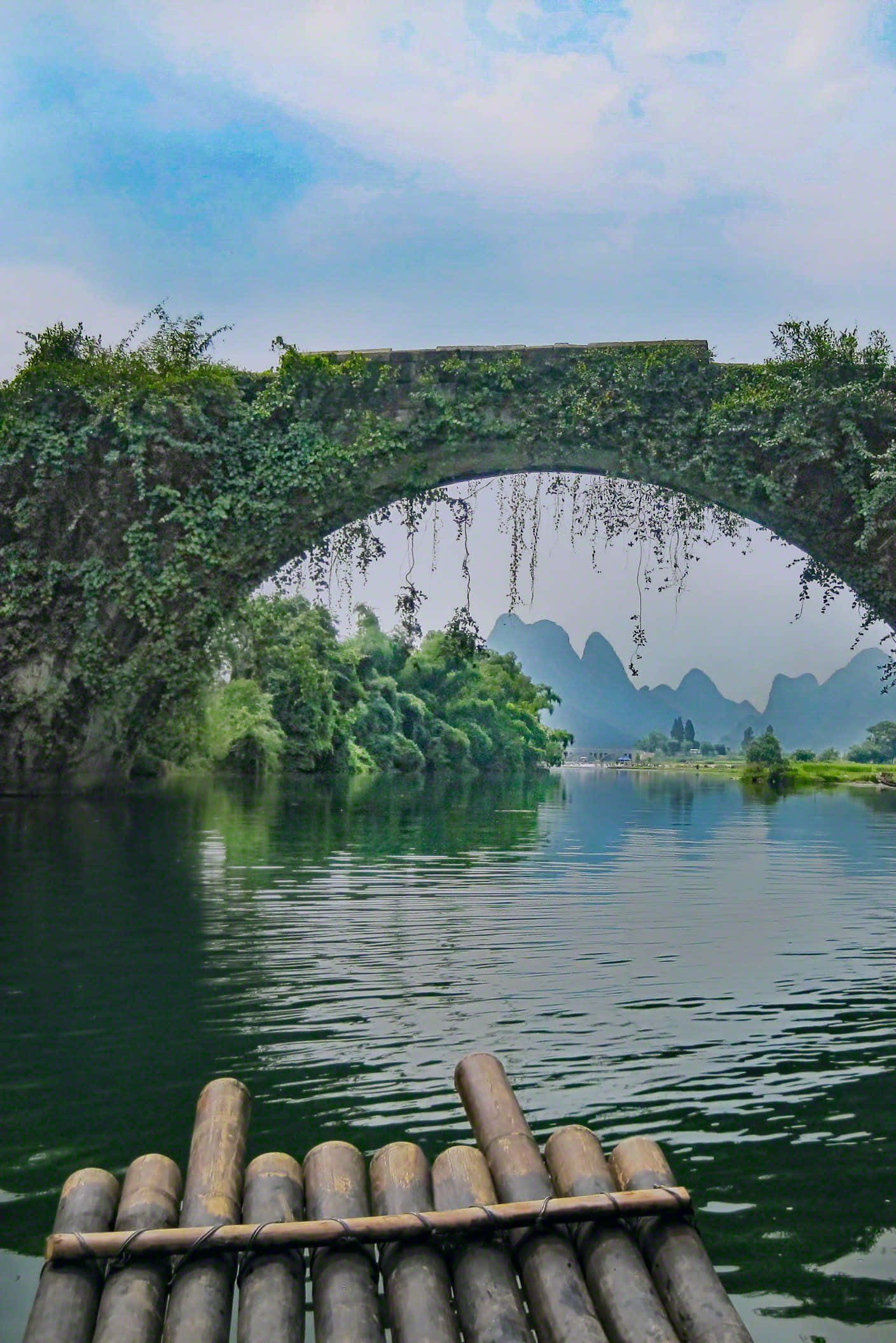 bridge 桌布 壁紙 — 竹筏漂浮在長滿青苔的石拱橋下，倒映在平靜的綠水中，遠處是喀斯特地貌的山巒。