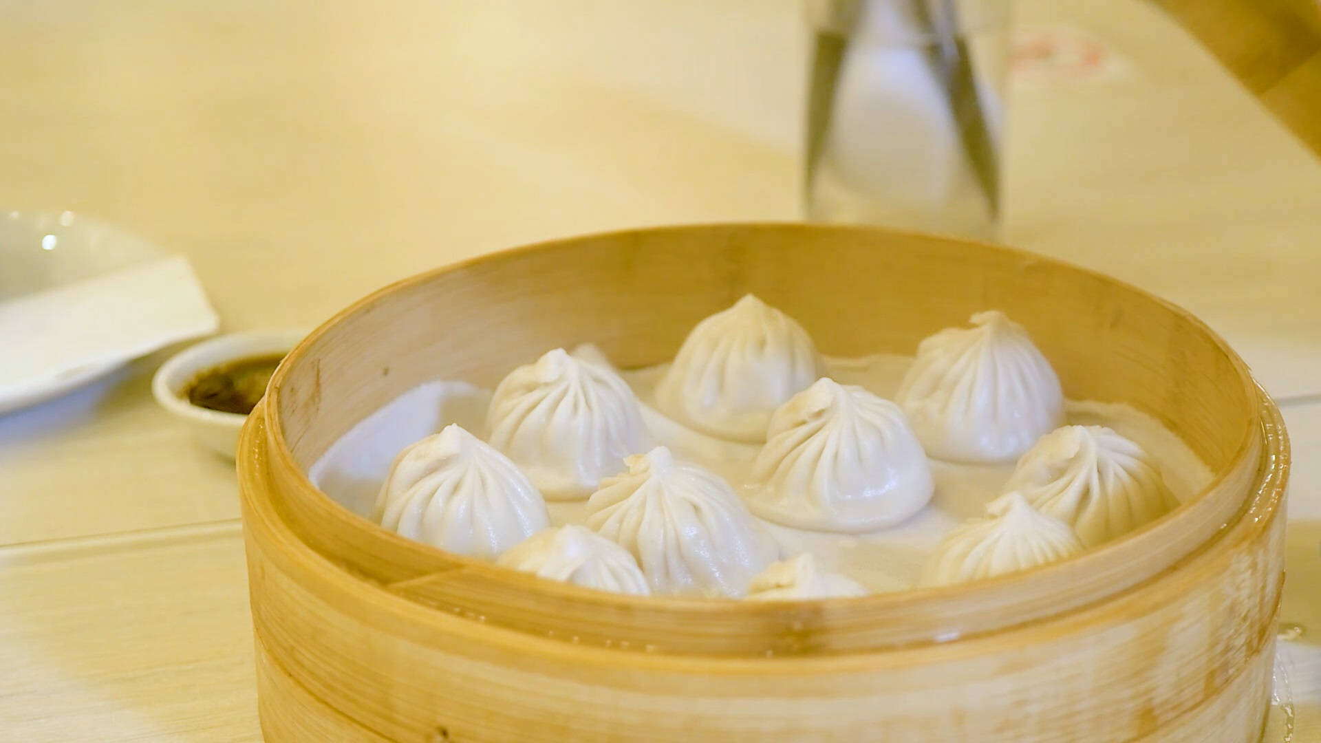 steam 桌布 壁紙 — 竹蒸籠裡裝滿了冒著蒸汽的餃子，放在木桌上，旁邊有蘸醬。