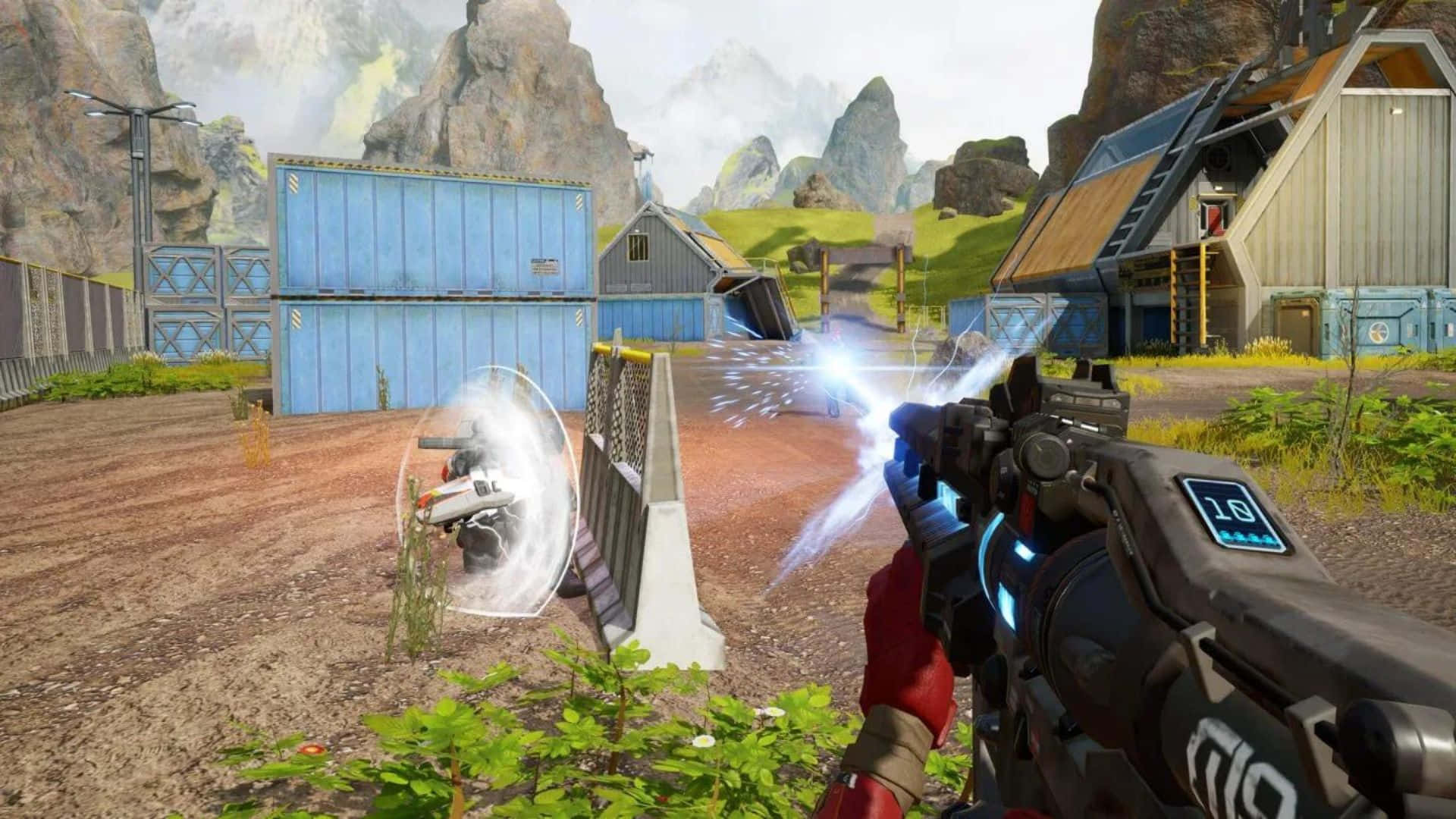 Fps Games 桌布 壁紙 — 第一人稱射擊遊戲畫面，顯示一把發光的能量武器向一個被力場包裹的無人機射擊，附近有工業貨櫃和岩石地形。