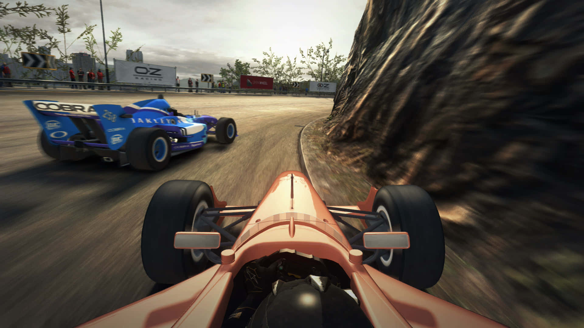 Grid Autosport 桌布 壁紙 — 第一人稱視角，一輛橙色賽車在岩石懸崖旁的蜿蜒賽道上加速超越藍色對手。