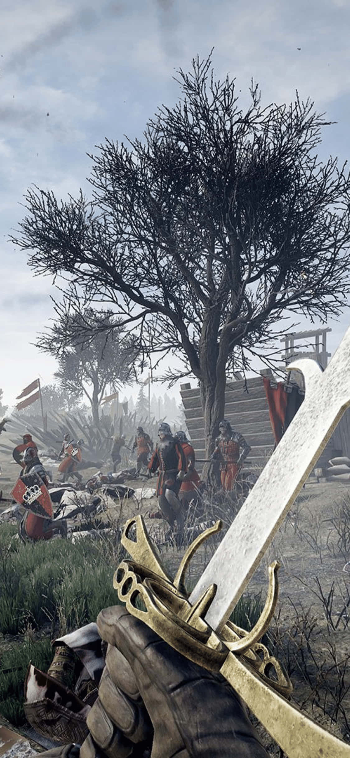 iPhone Xs Mordhau 桌布 壁紙 — 第一人稱視角，戴手套的手握著一把裝飾華麗的金色劍柄的劍，面對著有士兵和一棵光禿禿的樹的戰場，天空陰沉。
