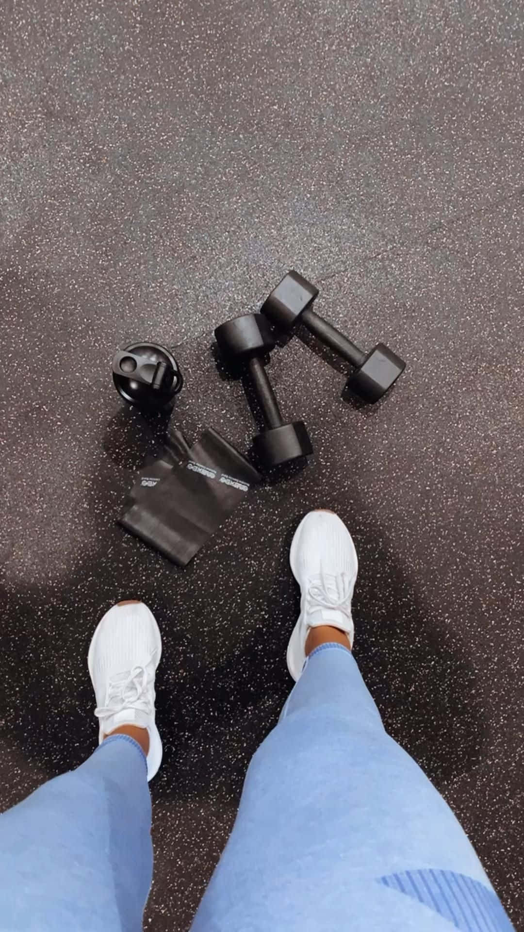 Dumbbell 桌布 壁紙 — 第一人稱視角，白色運動鞋中的腳站在黑色啞鈴和水瓶旁邊，地板是斑點健身房地板。