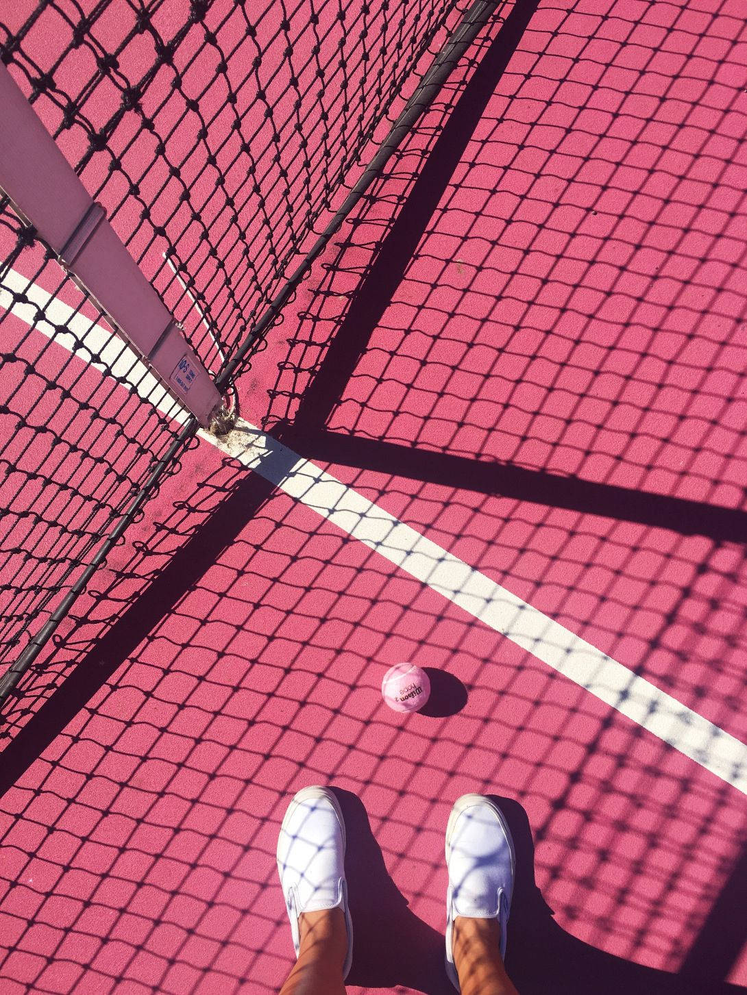 Tennis Ball 桌布 壁紙 — 第一人稱視角，白色鞋子站在充滿活力的粉紅色網球場上，球和網投下清晰的陰影。