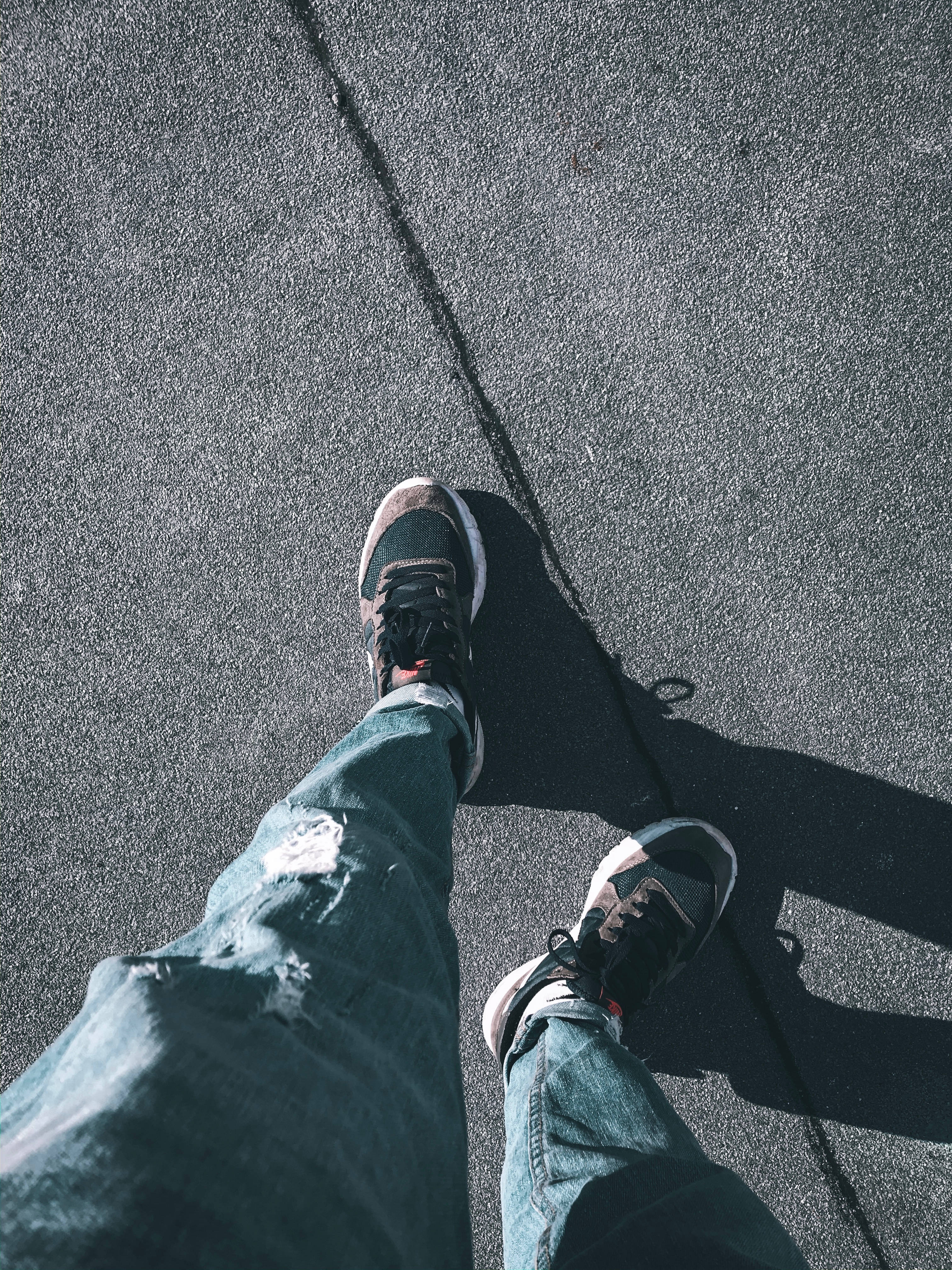 4K nike 桌布 壁紙 — 第一人稱視角，磨損的運動鞋和破洞牛仔褲踩在烈日下龜裂的柏油路上。