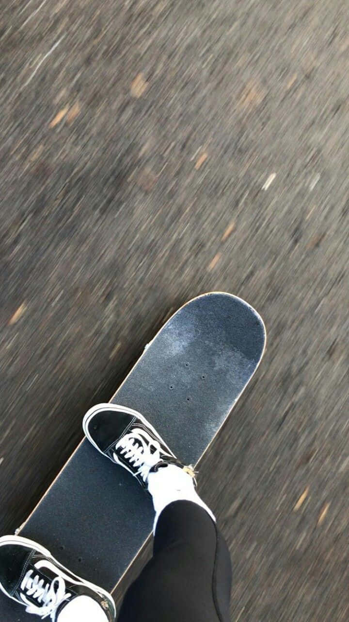 Retro Skateboard 桌布 壁紙 — 第一人稱視角，腳穿黑白運動鞋踩滑板沿著紋理瀝青路滑行，帶有動態模糊效果。