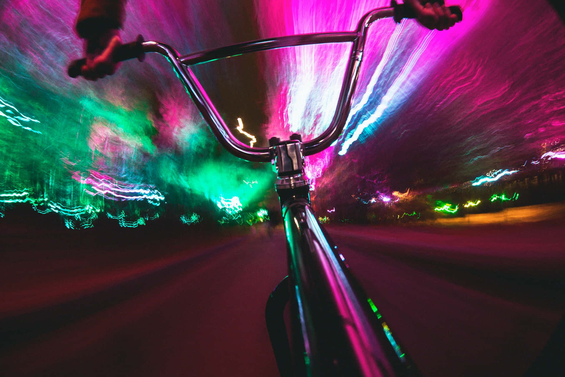 Psychedelic Neon Lights 桌布 壁紙 — 第一人稱視角，腳踏車在霓虹燈閃爍的都市夜晚中疾馳，帶有粉紅、綠色和藍色的光條。