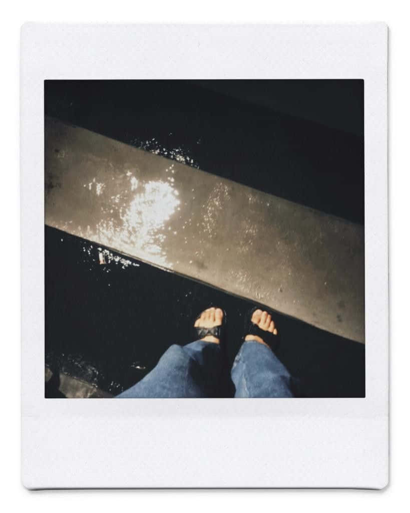 Aesthetic Polaroid 桌布 壁紙 — 第一人稱視角，赤腳穿著涼鞋站在濕漉漉的混凝土邊緣，下方水面反射出明亮的光線。