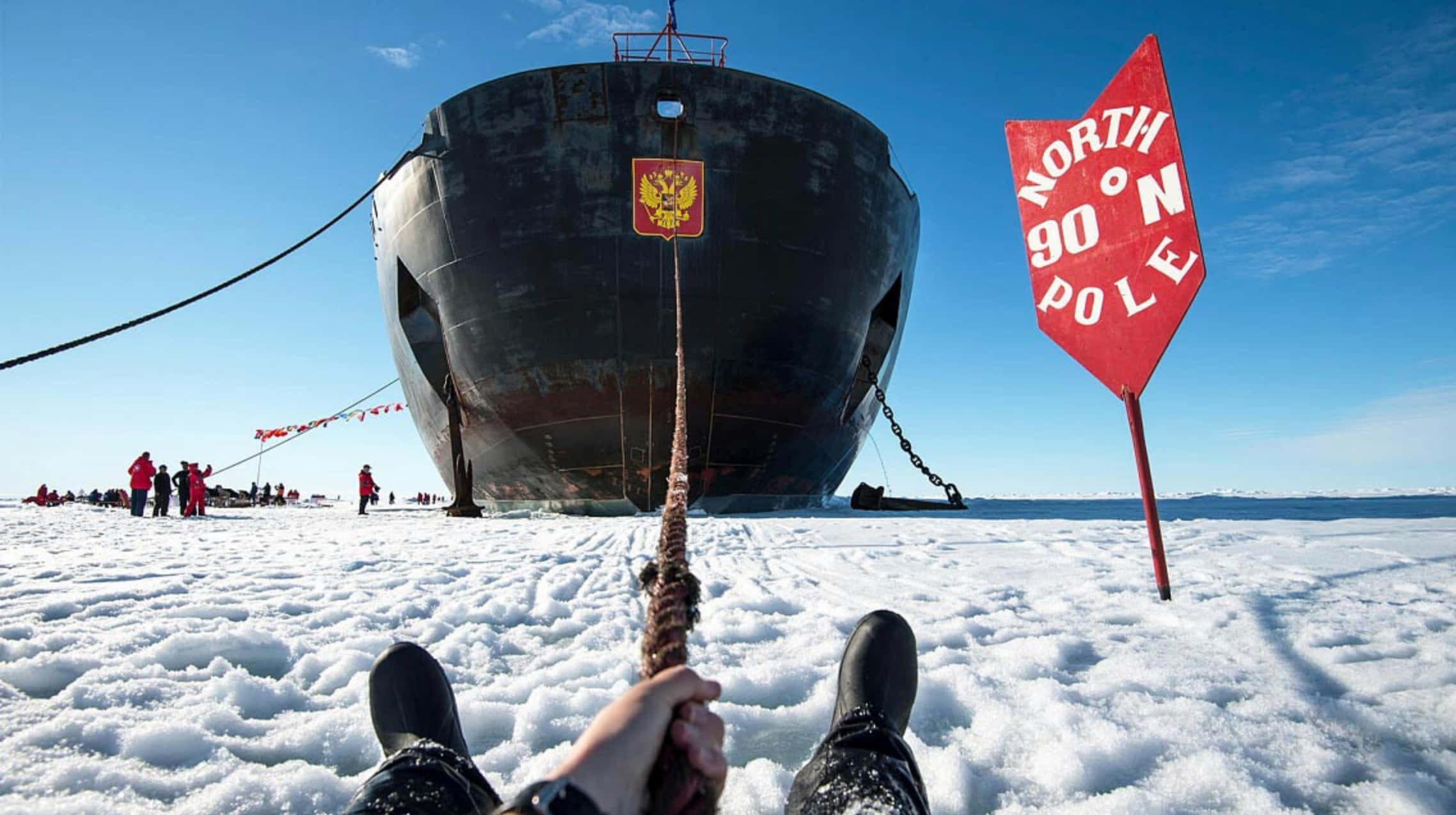 North Pole 桌布 壁紙 — 第一人稱視角，雙腳抓緊一條繫在停泊於北極的巨大船隻上的繩索，紅色標誌標示北緯90度。