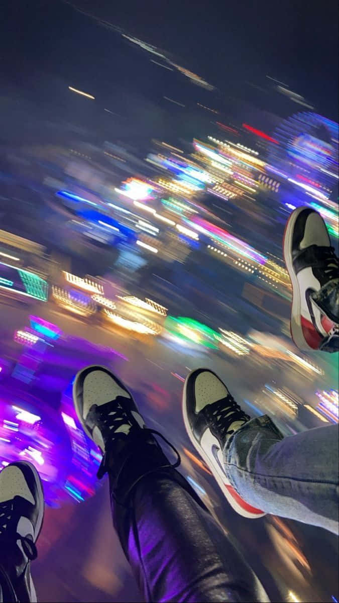 穿著運動鞋的雙腳懸掛在模糊的霓虹城市上方，夜晚。 — 鞋子 GIF 壁紙