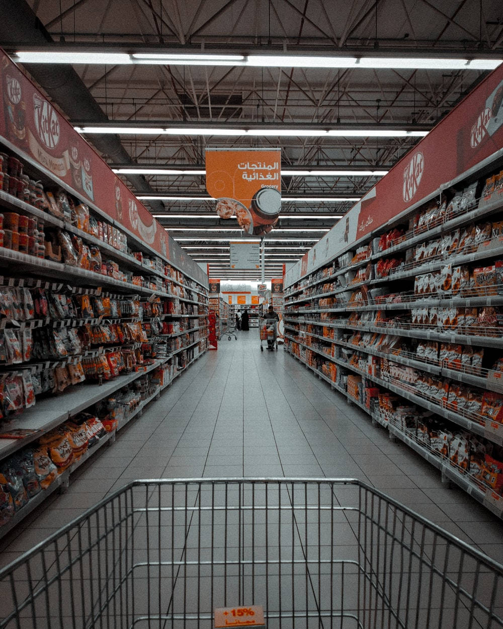Shopping 桌布 壁紙 — 第一人稱視角沿著一條長長的超市走道，兩旁是零食貨架和阿拉伯語標牌。