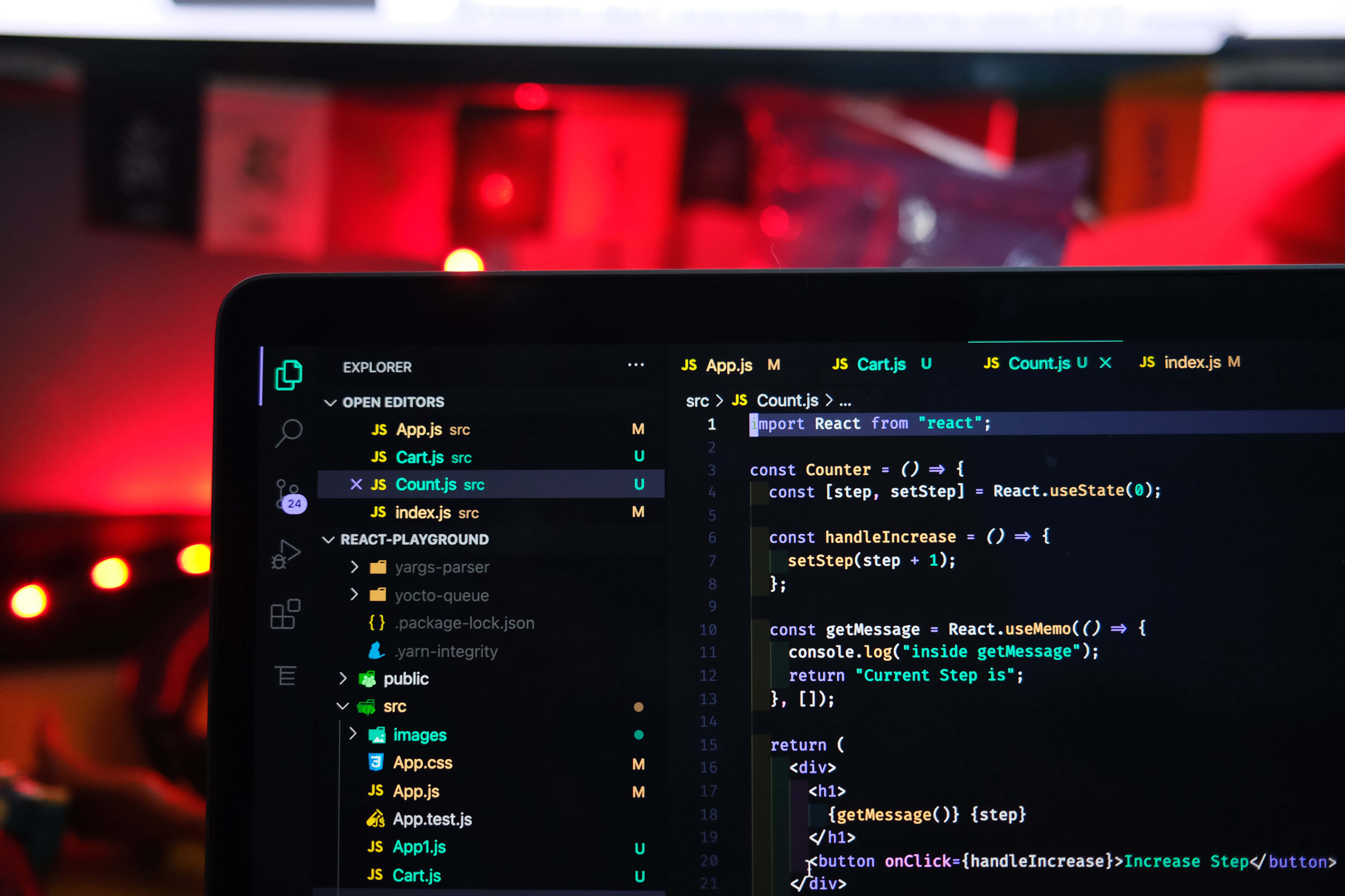 Code 桌布 壁紙 — 筆記型電腦在深色編輯器中顯示 React 程式碼，背景模糊的紅色燈光營造出舒適的科技工作空間。