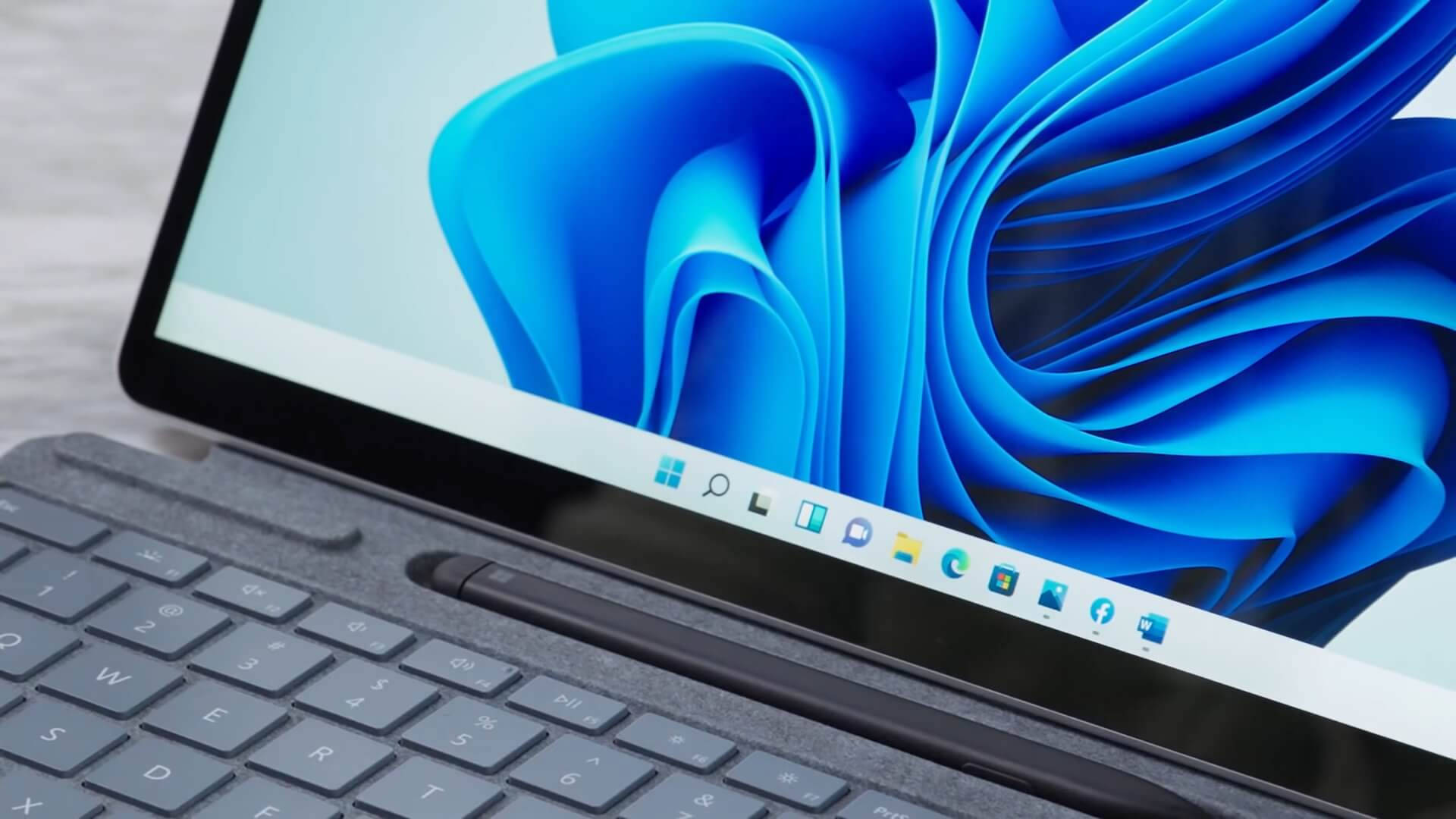 Windows 11 桌布 壁紙 — 筆記型電腦特寫，顯示帶有工作列圖示的動態藍色抽象桌布。