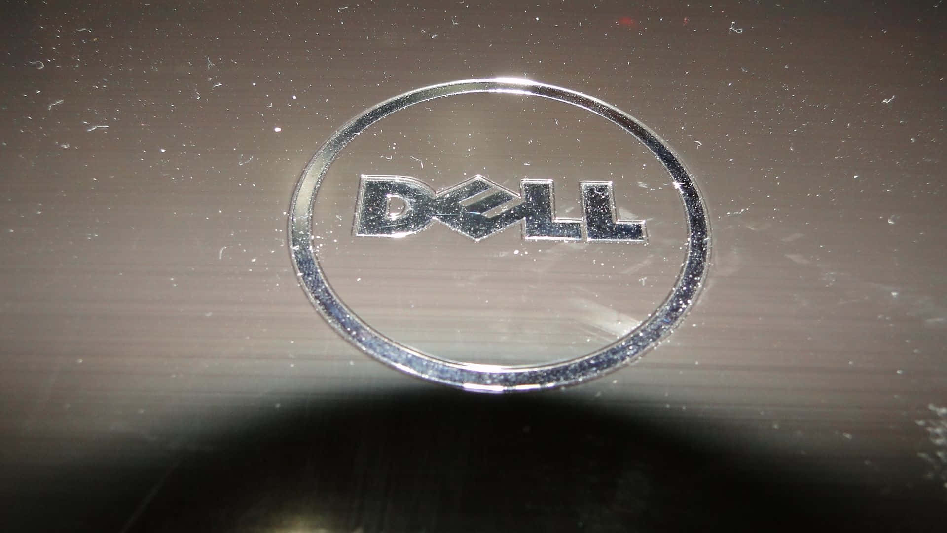 Dell 桌布 壁紙 — 筆記型電腦蓋上沾滿灰塵的銀色 Dell 標誌特寫，帶有可見的刮痕和污漬。