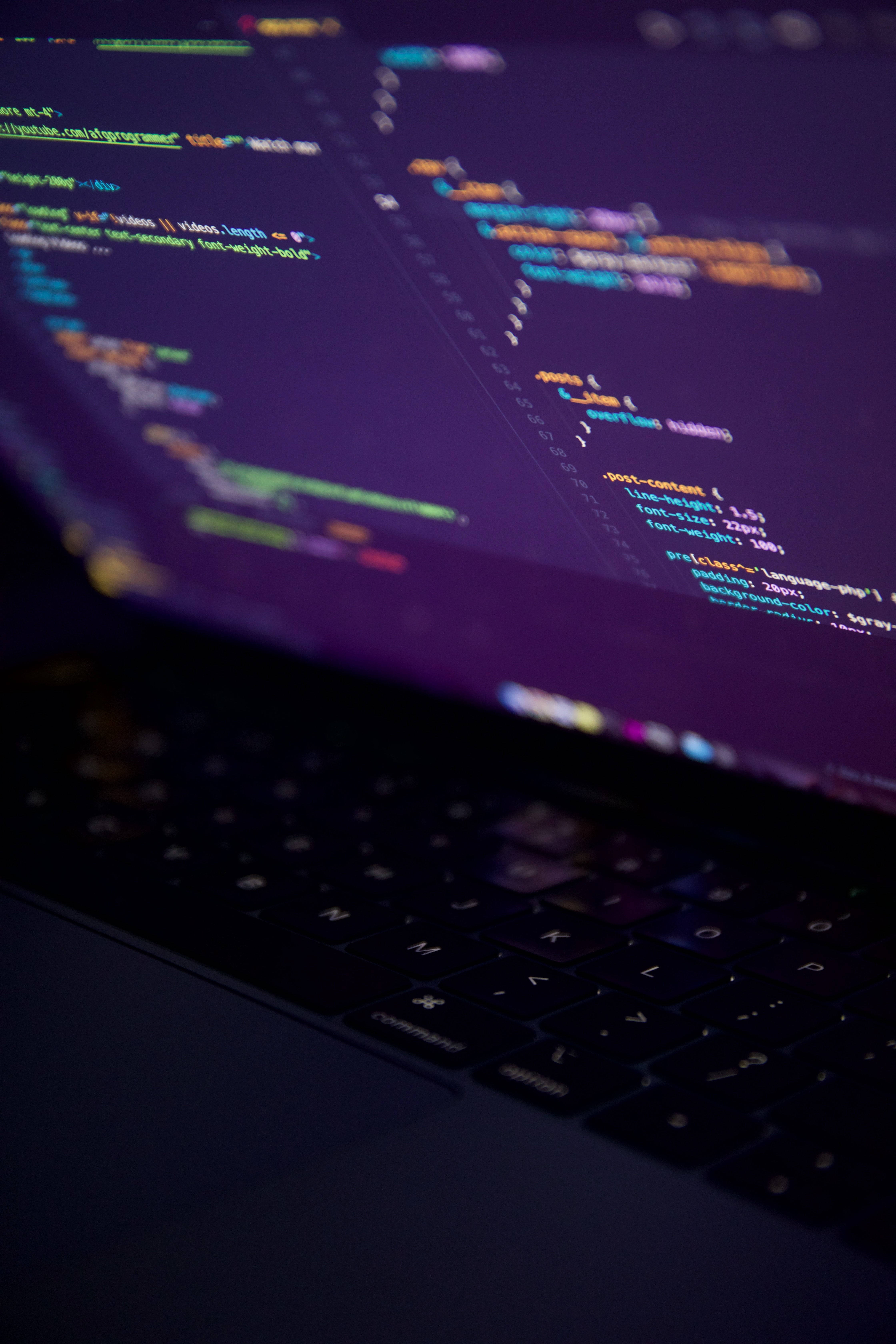 programming iPhone 桌布 壁紙 — 筆記型電腦螢幕特寫，顯示色彩繽紛的程式碼行，背景為深紫色，前景有模糊的鍵盤。