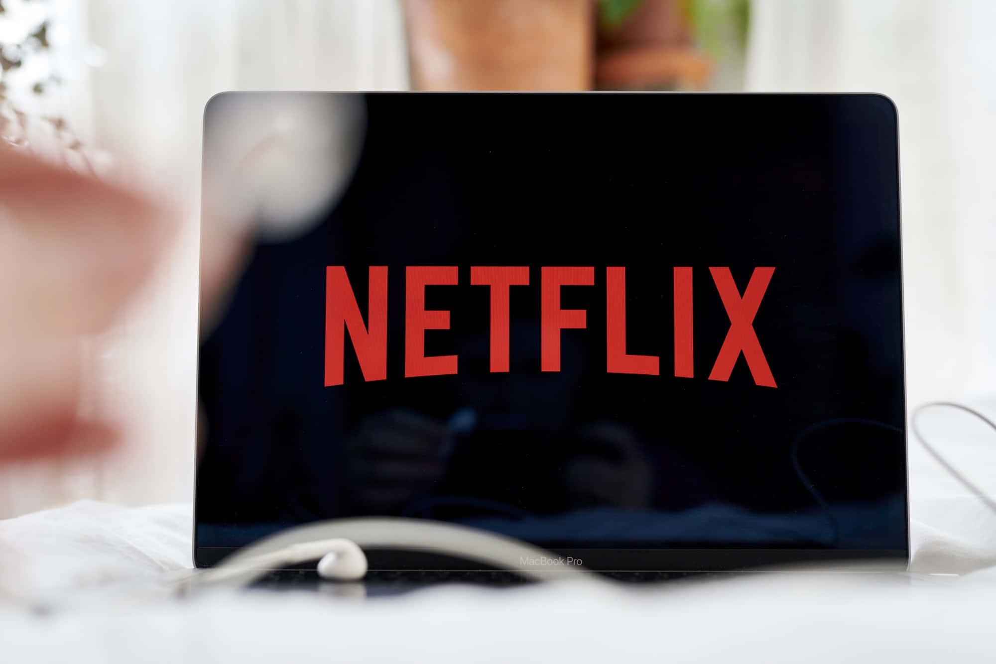 Netflix 桌布 壁紙 — 筆記型電腦螢幕顯示大膽的紅色Netflix標誌，背景為深色，周圍環境柔和模糊的室內場景。