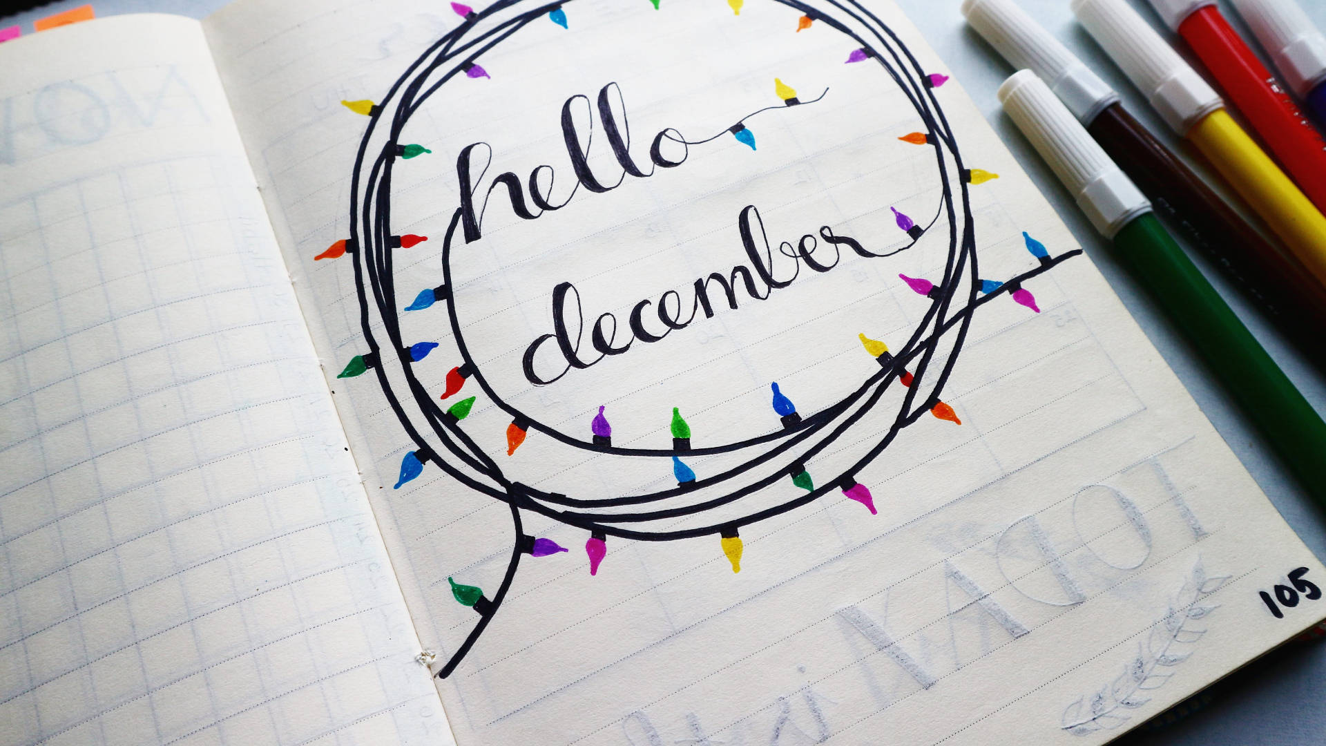 聖誕燈飾 桌布 壁紙 — 筆記本頁面以草書顯示「hello december」，周圍環繞著色彩繽紛的手繪燈串，附近有記號筆。
