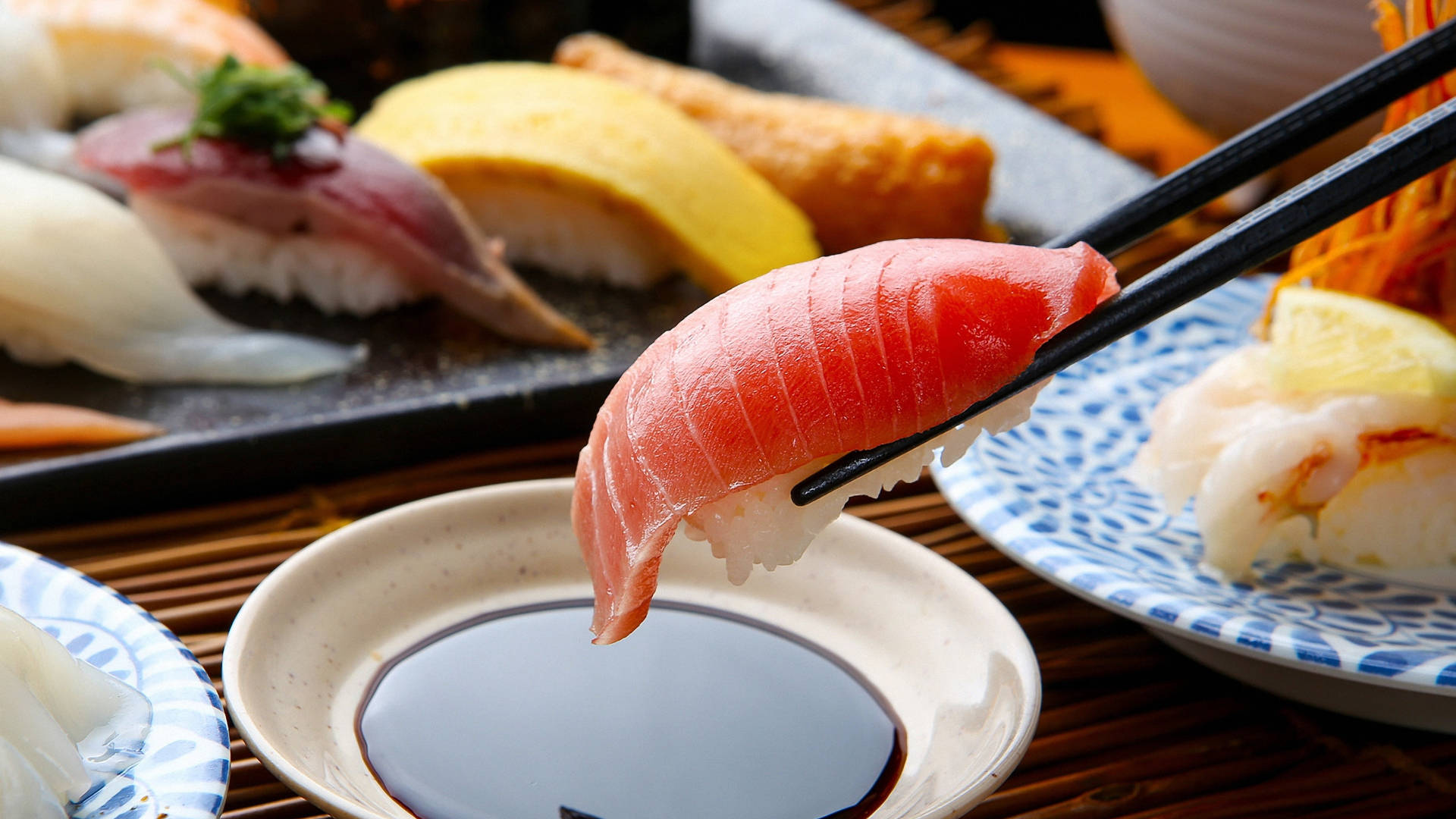 Sushi 桌布 壁紙 — 筷子夾起一片新鮮鮪魚握壽司，置於醬油碟上方，背景有各式壽司的特寫。