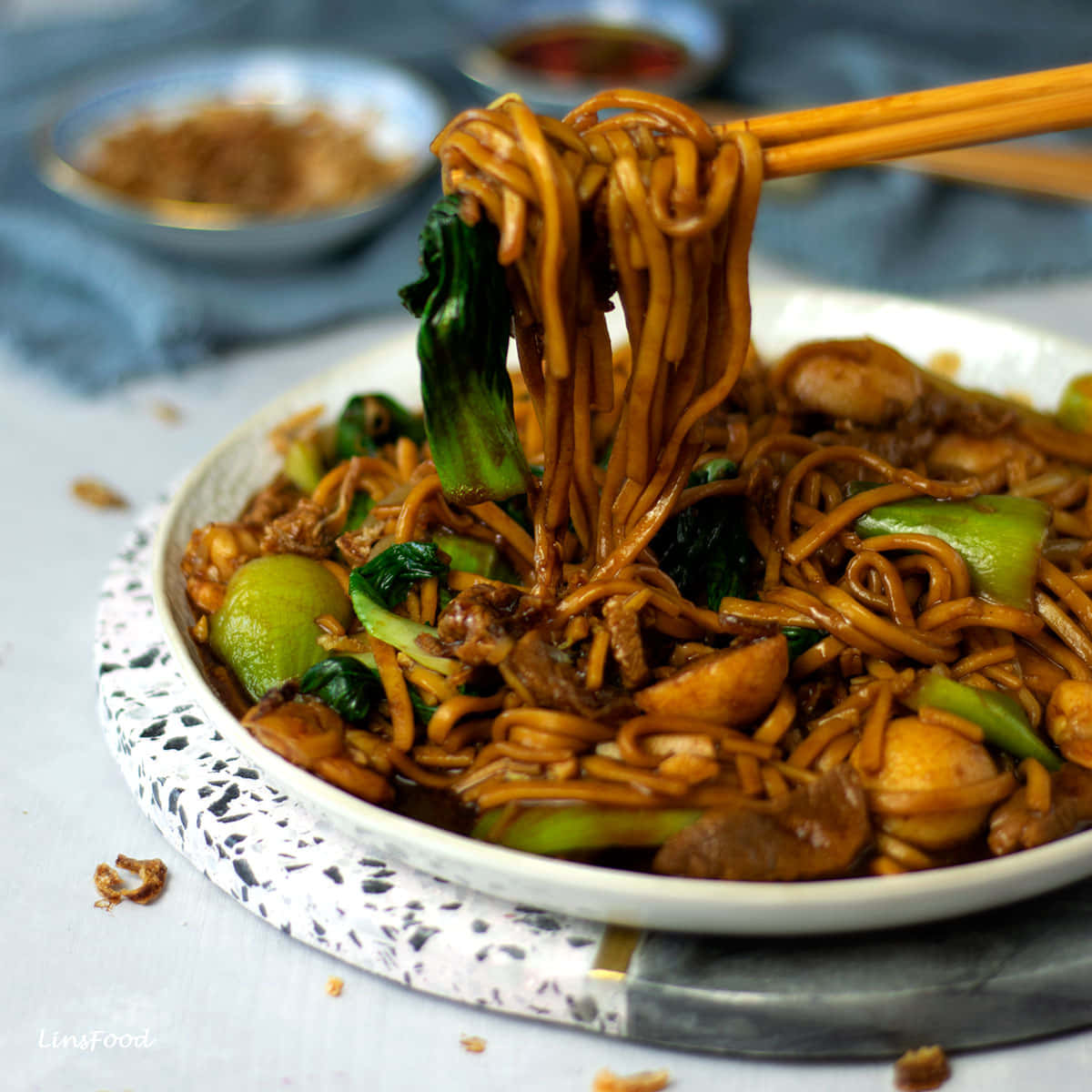 Tasty 桌布 壁紙 — 筷子從有斑點的白色碗中夾起亮澤的棕色麵條、綠色白菜和雞肉的近距離照片。