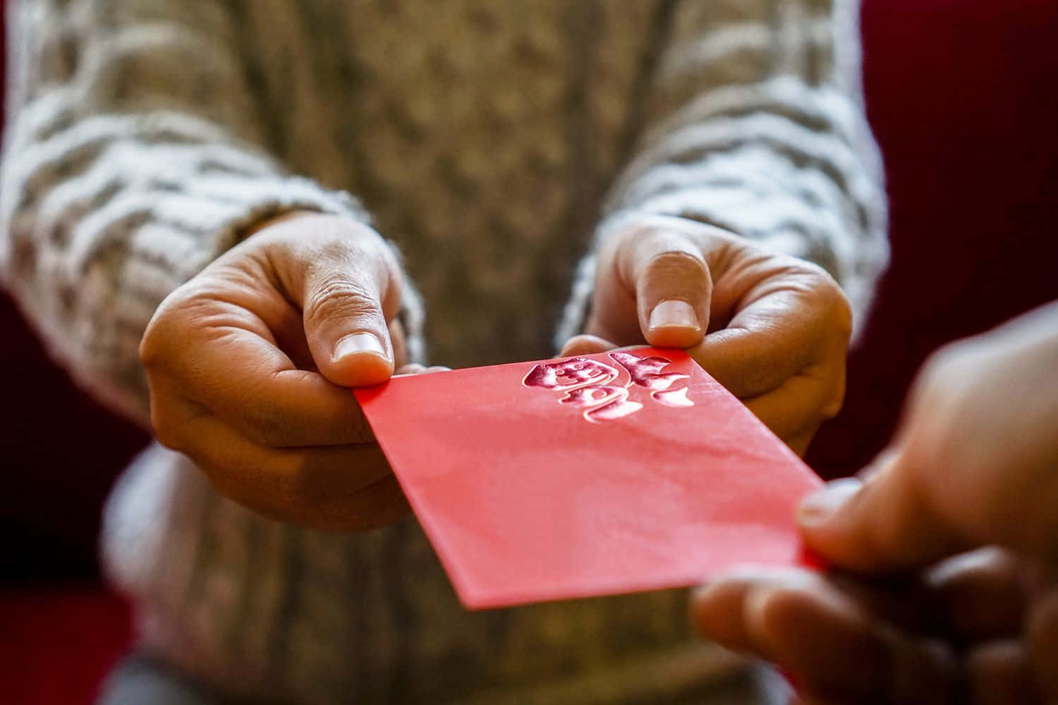 Red Envelope 桌布 壁紙 — 節日傳統中，雙手交換帶有金色中文字的紅色紅包的特寫。