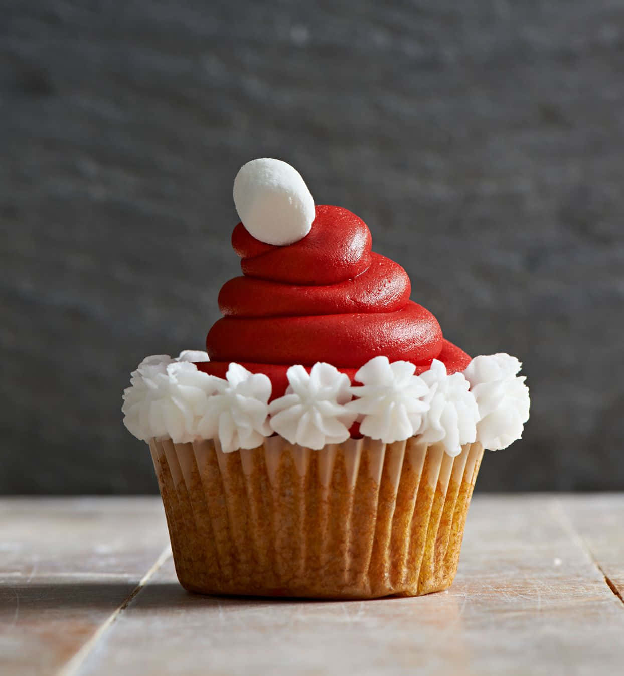 Cupcake 桌布 壁紙 — 節日紙杯蛋糕，頂部有紅色糖霜製成的聖誕老人帽形狀，白色裱花糖霜和棉花糖絨球。