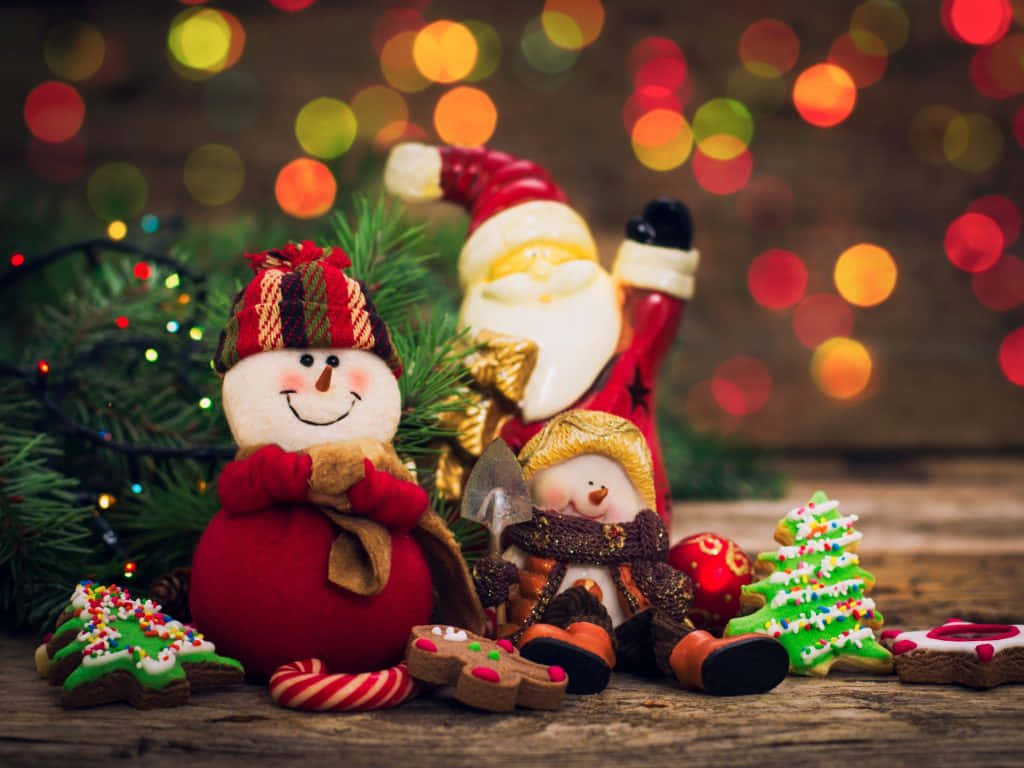 Red Christmas 桌布 壁紙 — 節日聖誕公仔包括雪人和聖誕老人，周圍有薑餅餅乾和松樹枝，背景是溫暖的散景燈光。