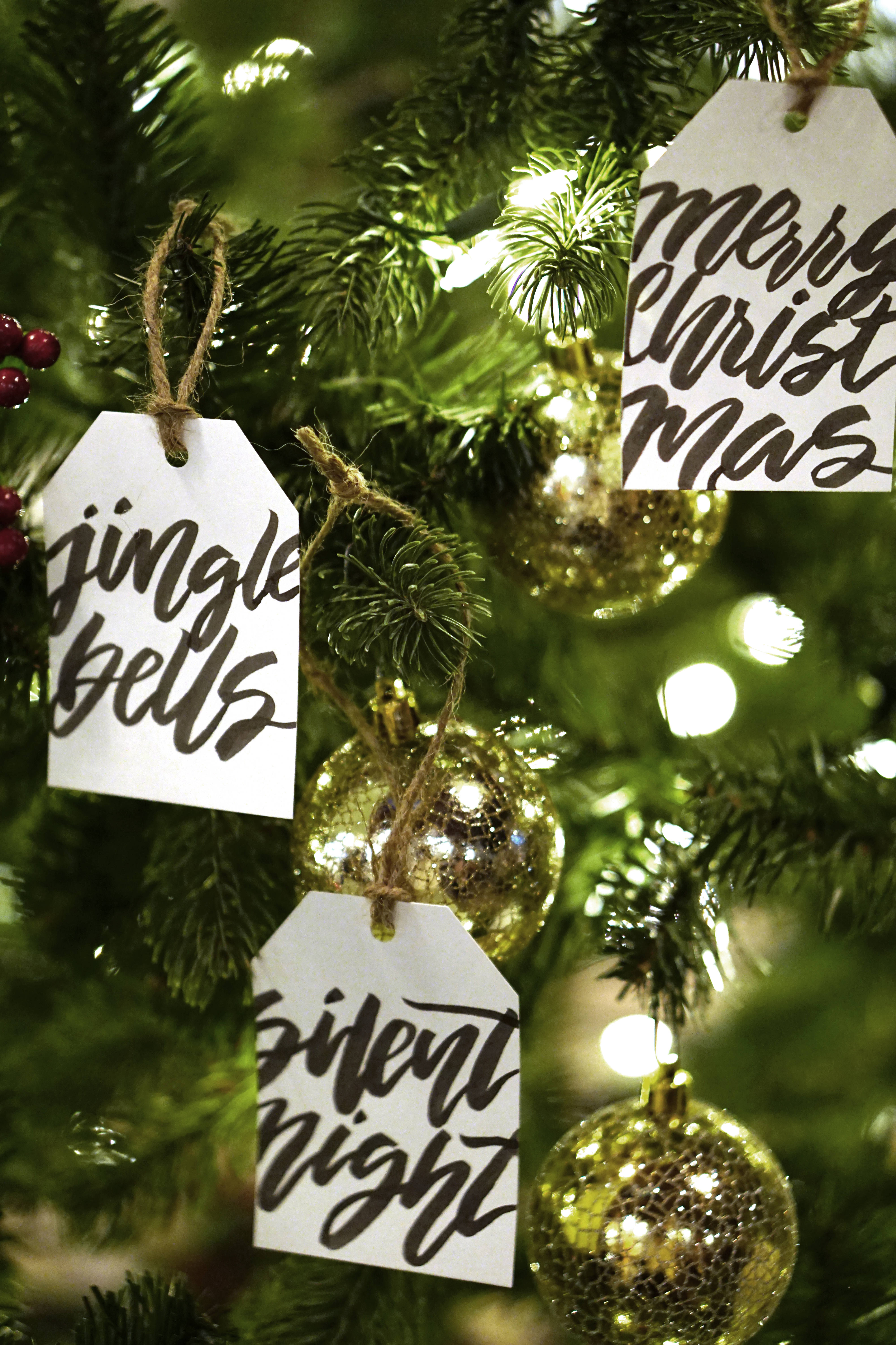 聖誕快樂 桌布 壁紙 — 節日聖誕樹標籤的特寫，上面寫著 jingle bells 聖誕快樂 平安夜，掛在綠色松針和金飾之間。