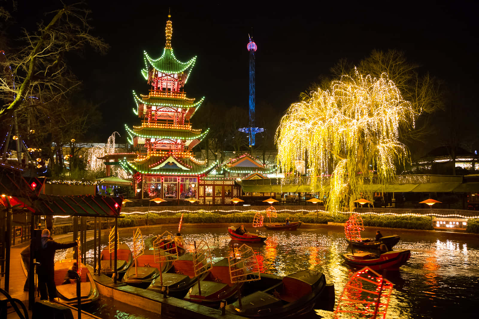 節日夜景，發光的寶塔和柳樹倒映在運河中，伴有船隻。
