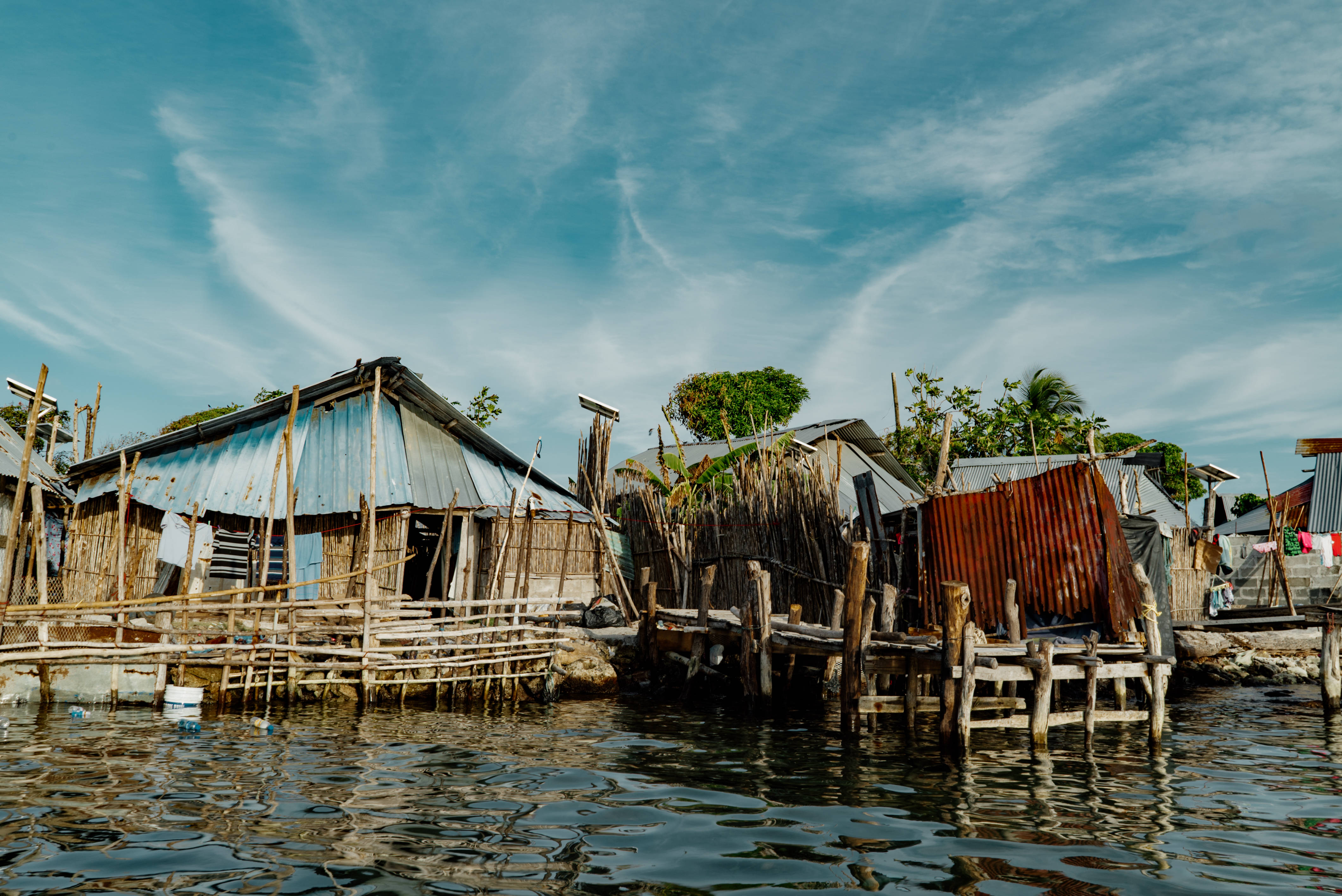 Panama 桌布 壁紙 — 簡樸的高腳屋，帶有波紋金屬屋頂，漂浮在平靜的水面上，上方是明亮的藍天和縷縷白雲。