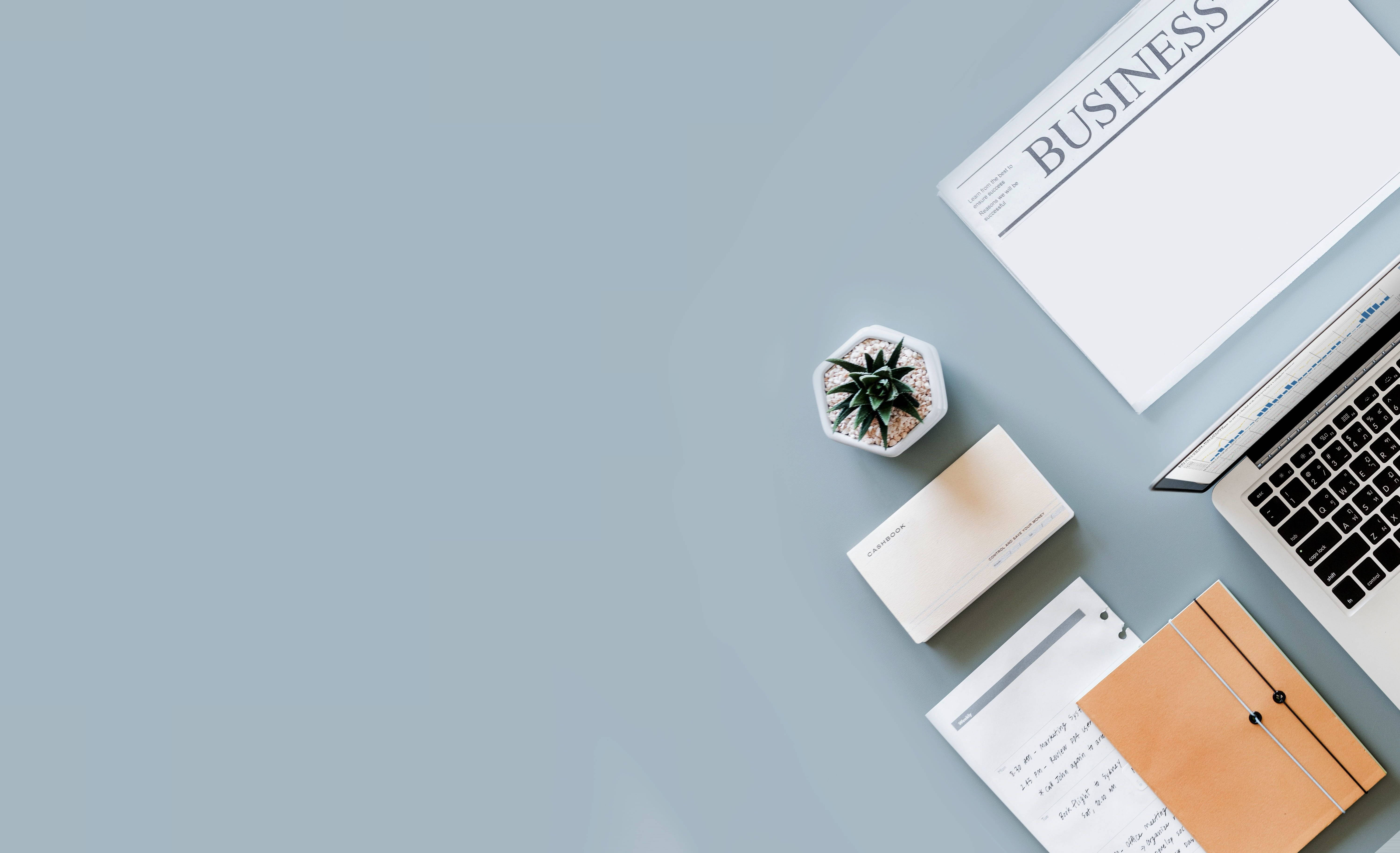 Business 桌布 壁紙 — 簡約俯視圖，展示一張乾淨的辦公桌，上面有手提電腦、商業雜誌、筆記本和小型多肉植物，置於柔軟的藍色表面上。
