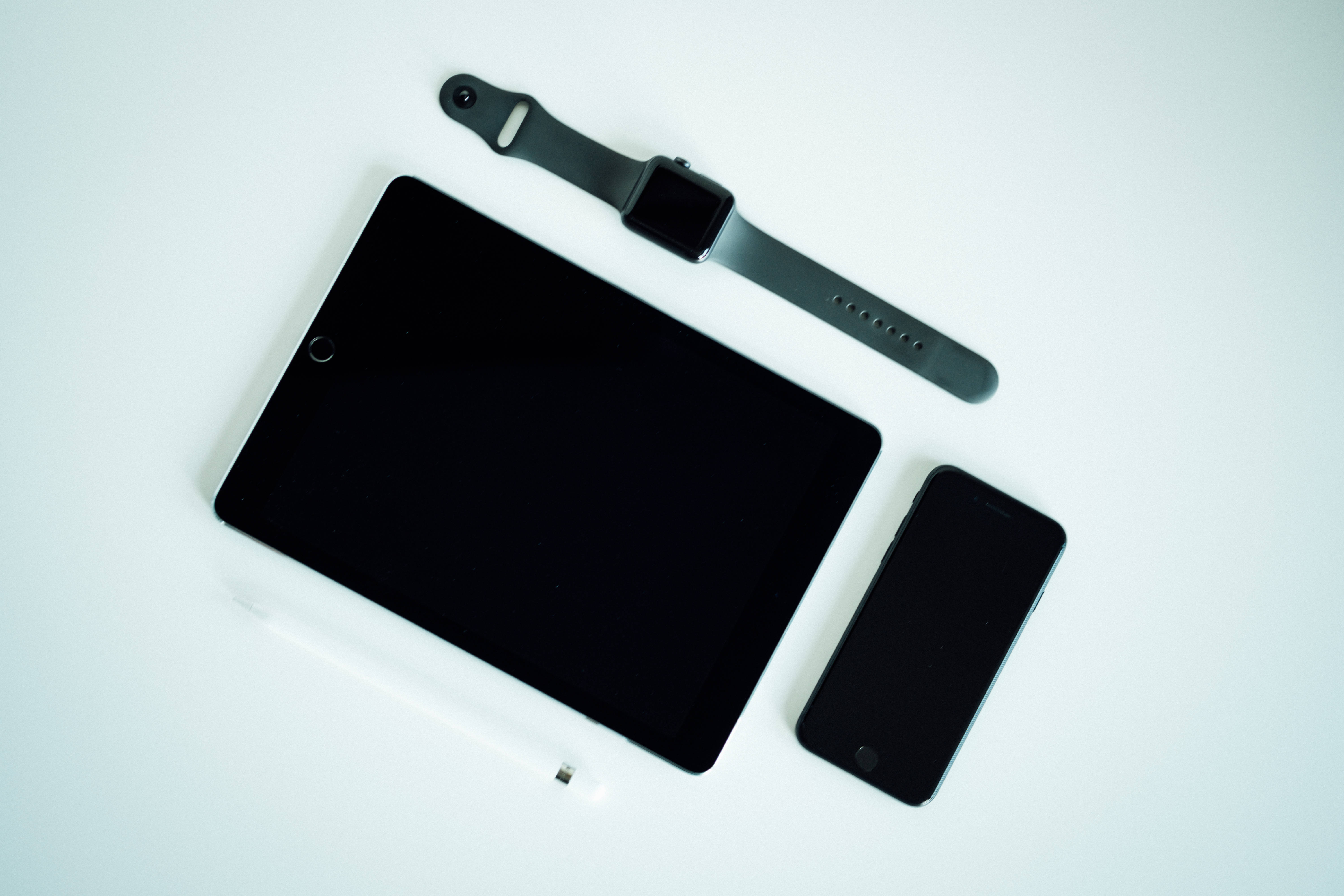 Apple iPad Pro 桌布 壁紙 — 簡約平鋪擺拍：黑色平板電腦、智慧手錶和手機，搭配白色觸控筆，置於潔白表面上。