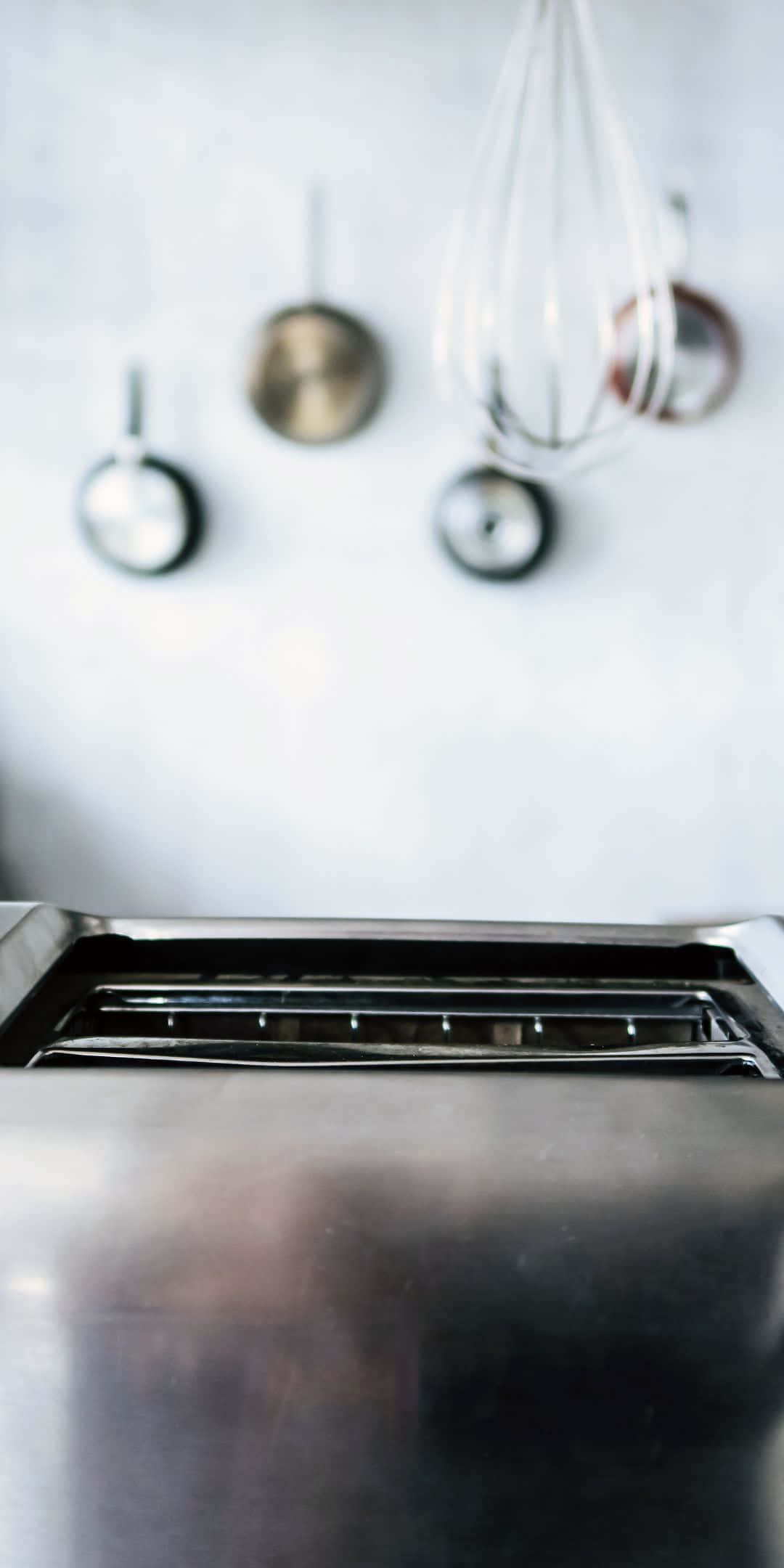 Pixel 3 Kitchen 桌布 壁紙 — 簡約廚房前景中一個時尚的不鏽鋼烤麵包機，背景有模糊的掛鍋和打蛋器。