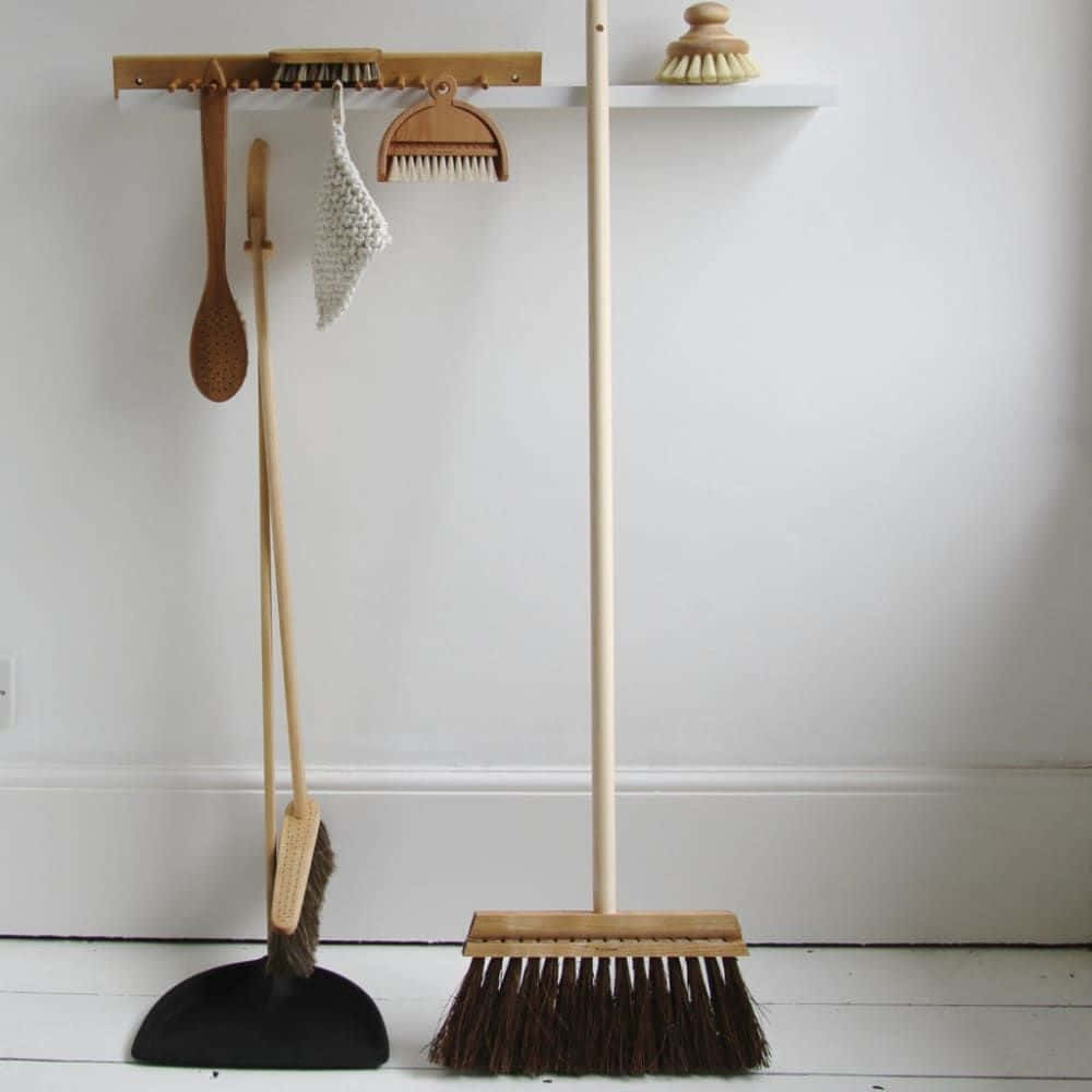 Cleaning 桌布 壁紙 — 簡約木製清潔工具整齊地掛在白色牆架上，下方白色地板上有相配的掃帚和簸箕。