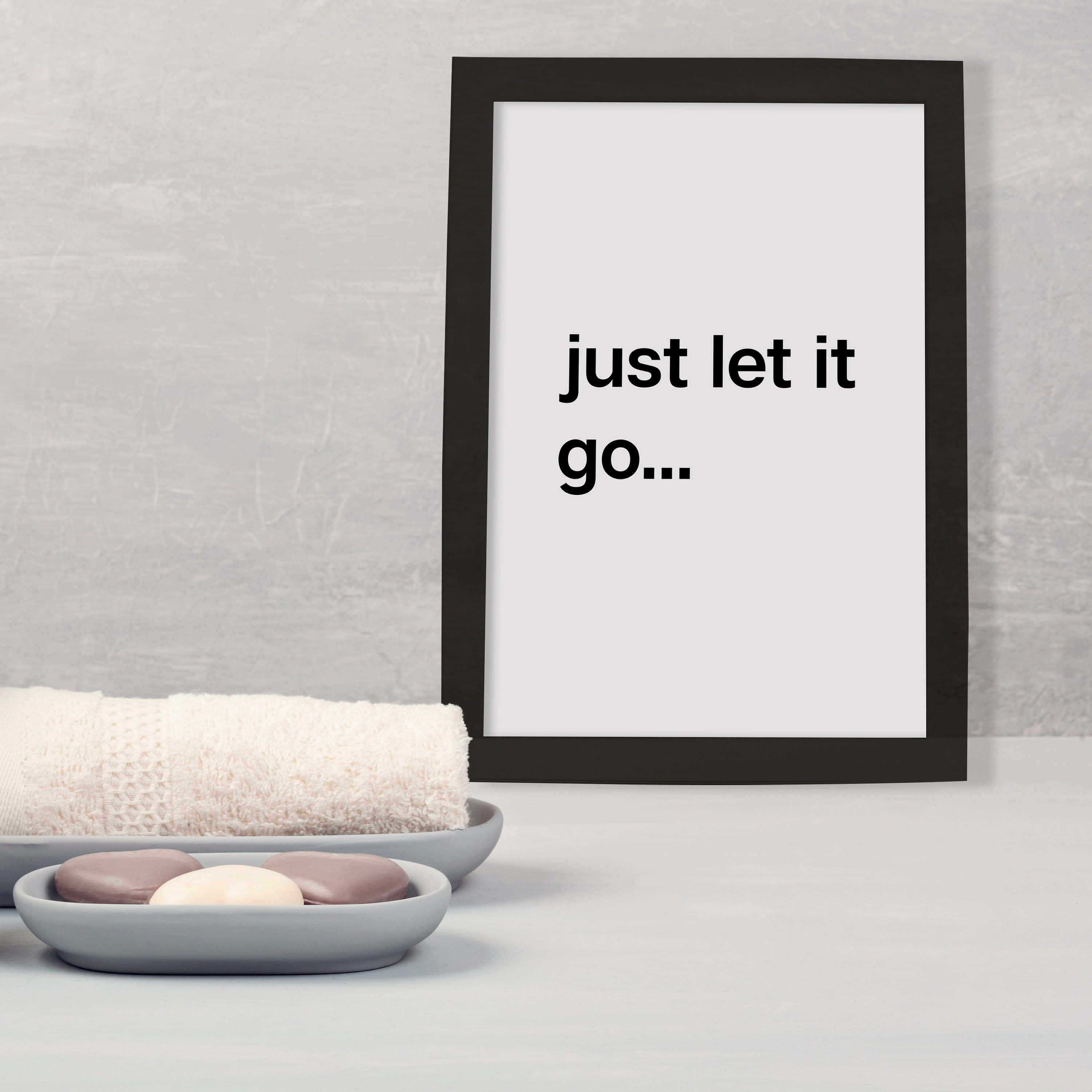 let it go 桌布 壁紙 — 簡約浴室場景，配有裱框勵志語錄，旁邊是捲起的毛巾和肥皂碟。