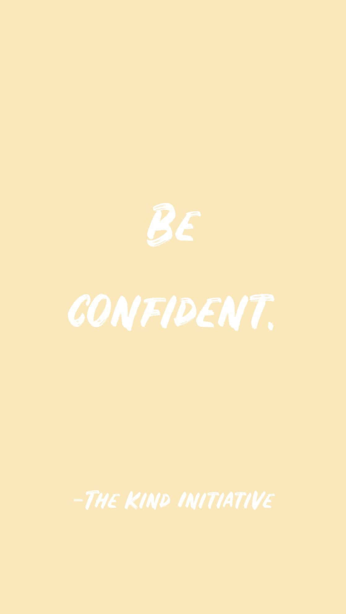 Quote 桌布 壁紙 — 簡約淡黃色背景，白色刷筆文字寫著「BE CONFIDENT」和下方的「-THE KIND INITIATIVE」。