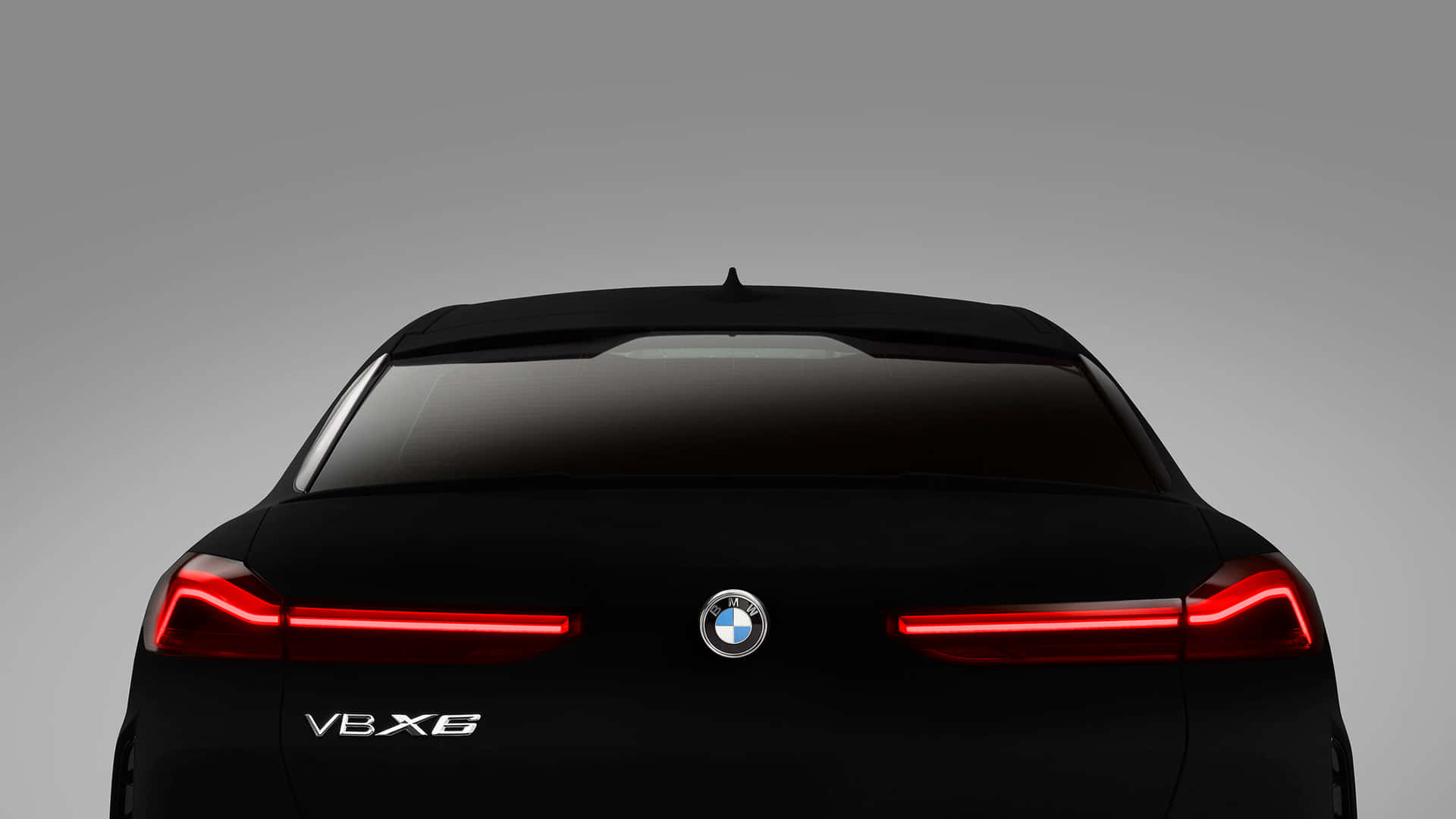 Vantablack 桌布 壁紙 — 簡約灰色背景上，一輛時尚黑色BMW V8X6的後視圖，帶有發光的紅色尾燈。