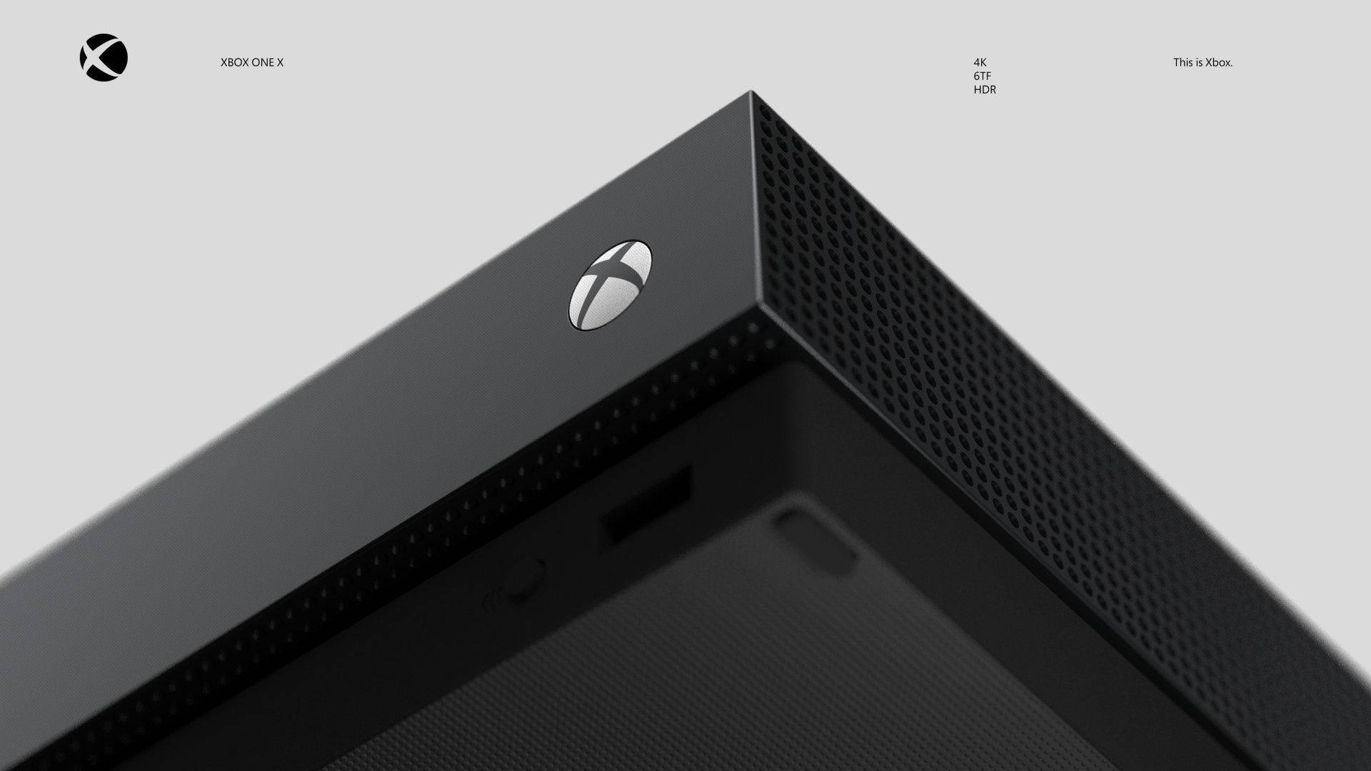 Xbox 桌布 壁紙 — 簡約灰色背景上，時尚黑色 Xbox One X 主機角落的特寫，帶有銀色標誌和穿孔紋理。