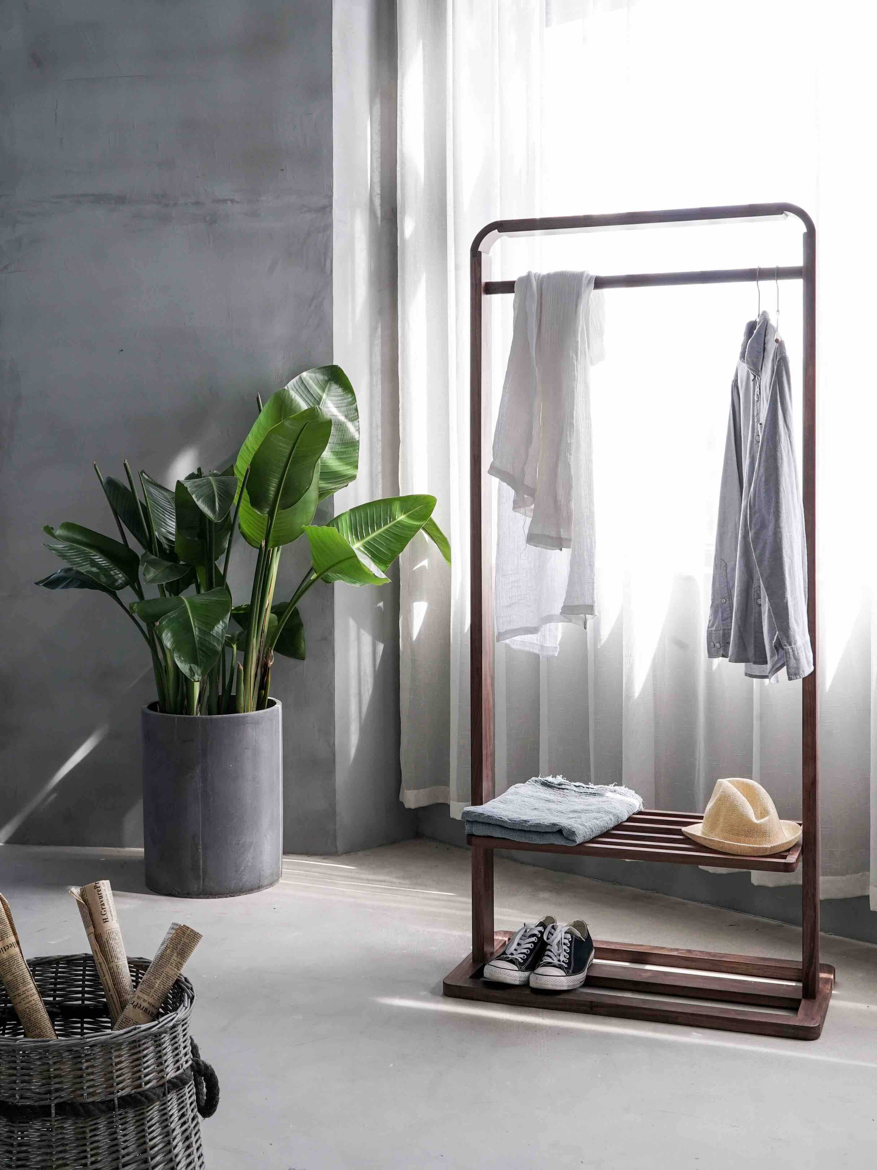 Trendy 桌布 壁紙 — 簡約現代房間角落，木製衣架掛著衣服和鞋子，旁邊有一棵大盆栽，靠近明亮的窗戶。