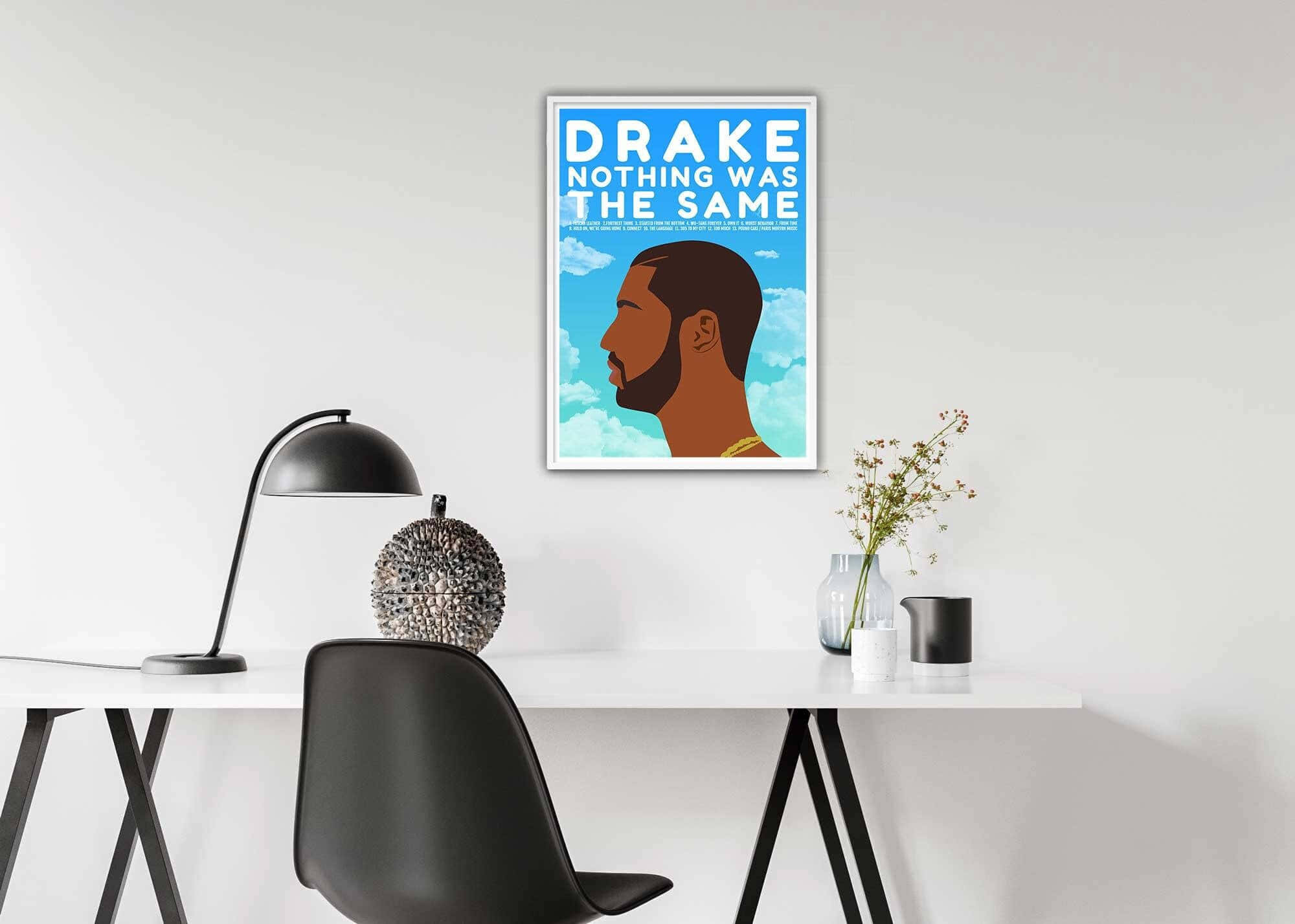 桌布 壁紙 — 簡約現代辦公桌設置，牆上掛著Drake專輯海報框，下方是時尚黑色椅子和燈。