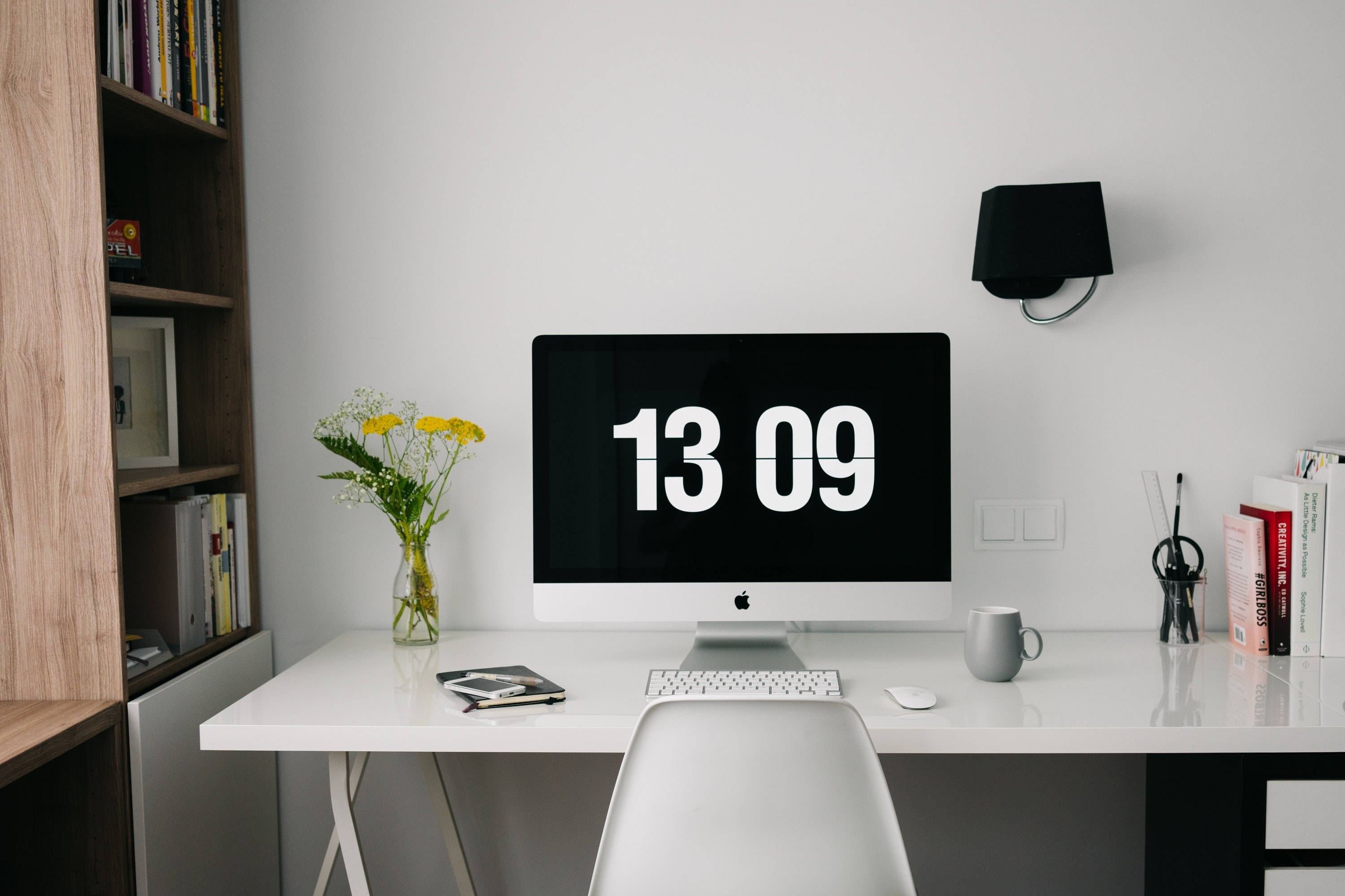 Mac 桌布 壁紙 — 簡約白色書桌，iMac 在黑色螢幕上顯示粗體白色數字 13 09，周圍環繞書籍、花瓶和現代椅子。