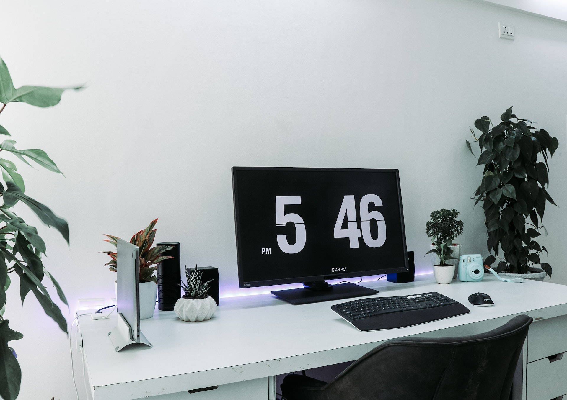 Office Space 桌布 壁紙 — 簡約白色書桌設置，配備顯示5:46 PM的數位時鐘，周圍環繞盆栽植物和科技小工具。