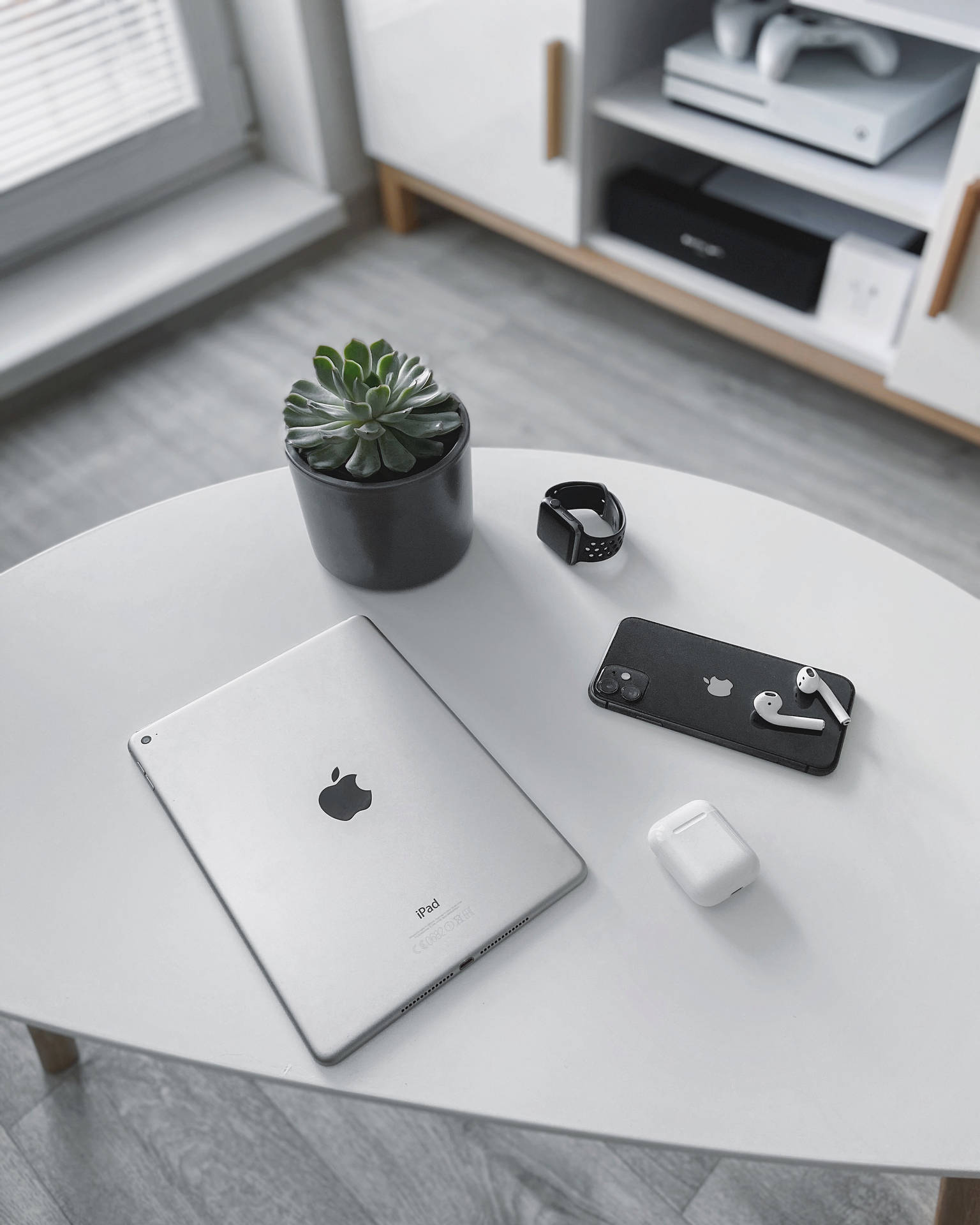 白色桌子上有iPad、電話、智慧手錶、耳機和多肉植物，在現代房間中。 — 4K iPad 壁紙 壁紙
