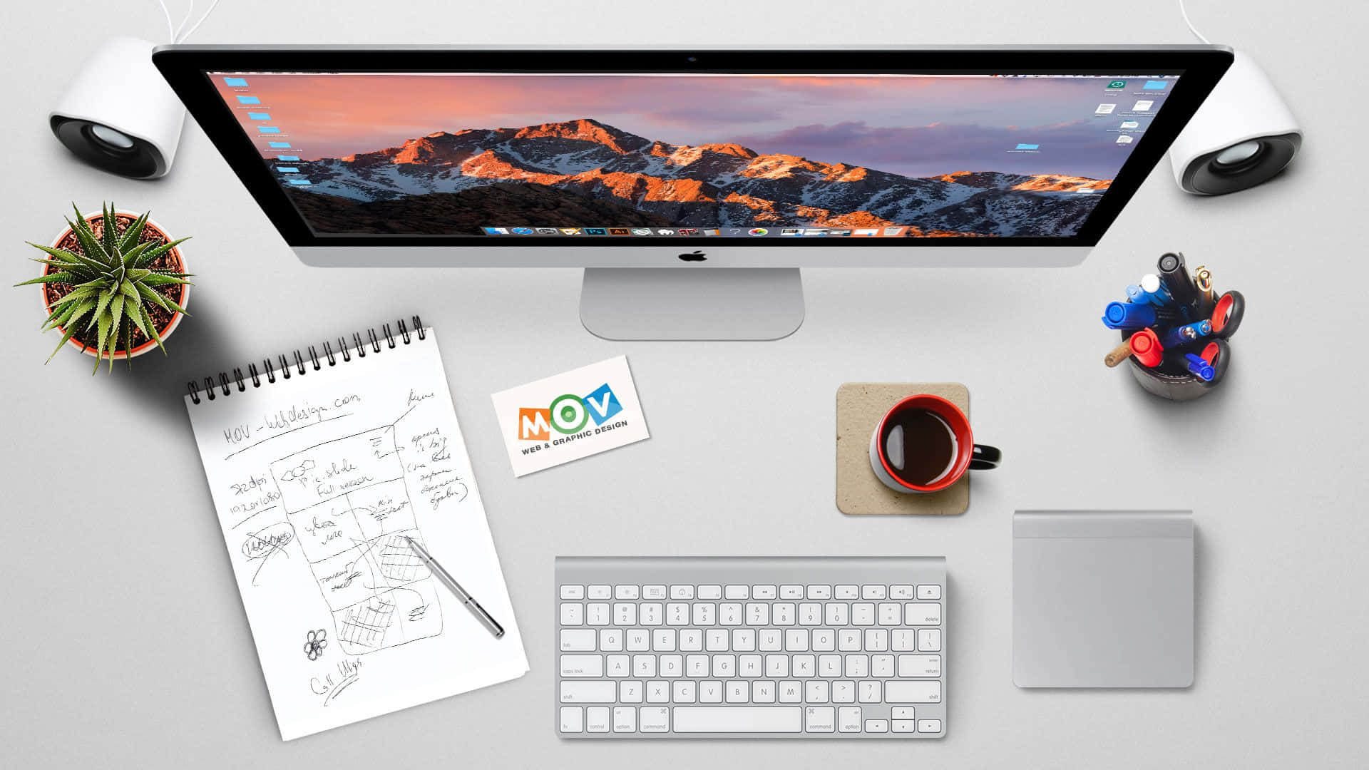 Website 桌布 壁紙 — 簡約白色桌面設置，iMac 顯示雪山日落桌布，周圍有咖啡、筆記本和喇叭。