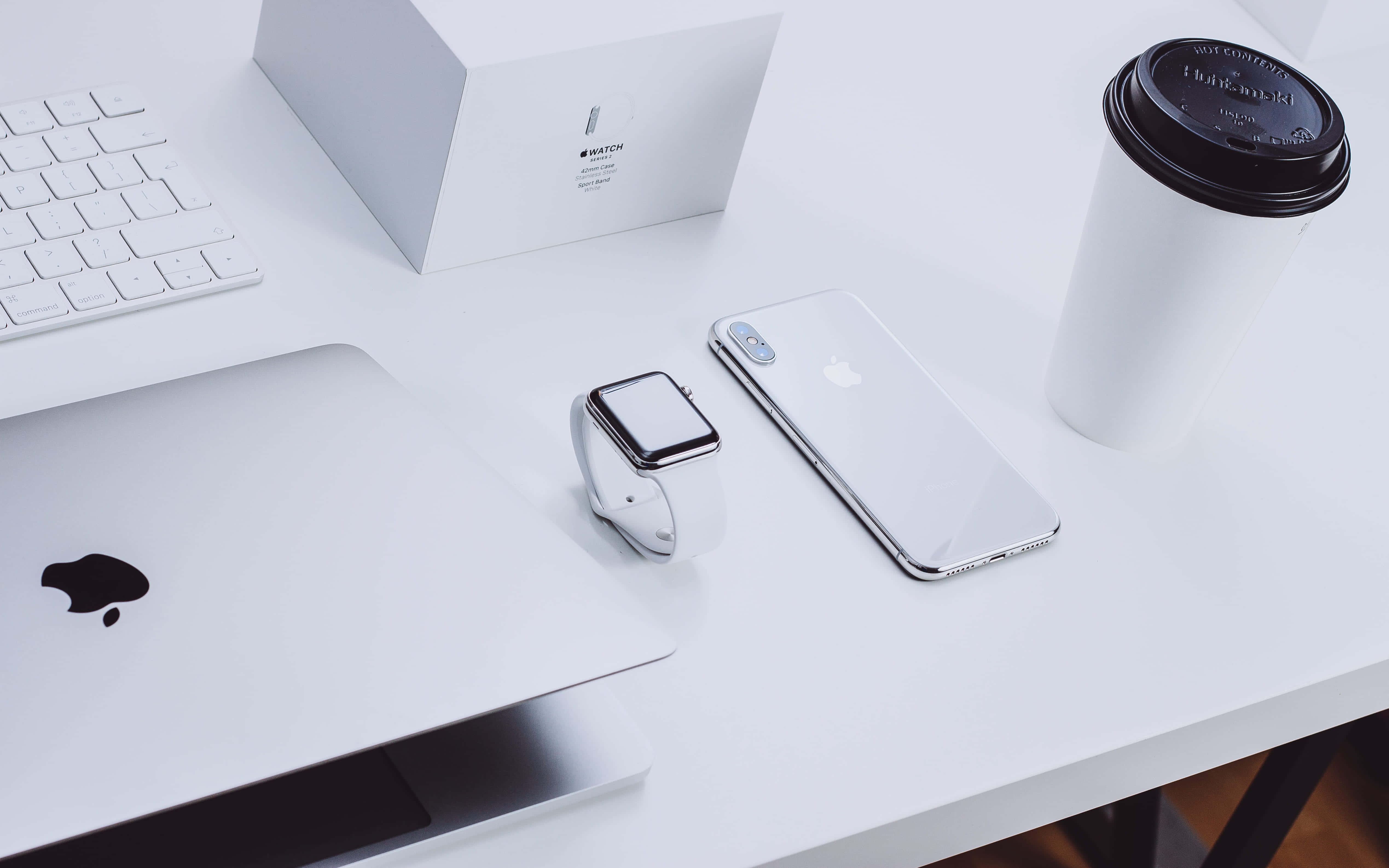 美學 MacBook 壁紙 桌布 壁紙 — 簡約白色桌面設置，配備Apple筆記型電腦、手錶、電話和咖啡杯，呈現乾淨現代美學。