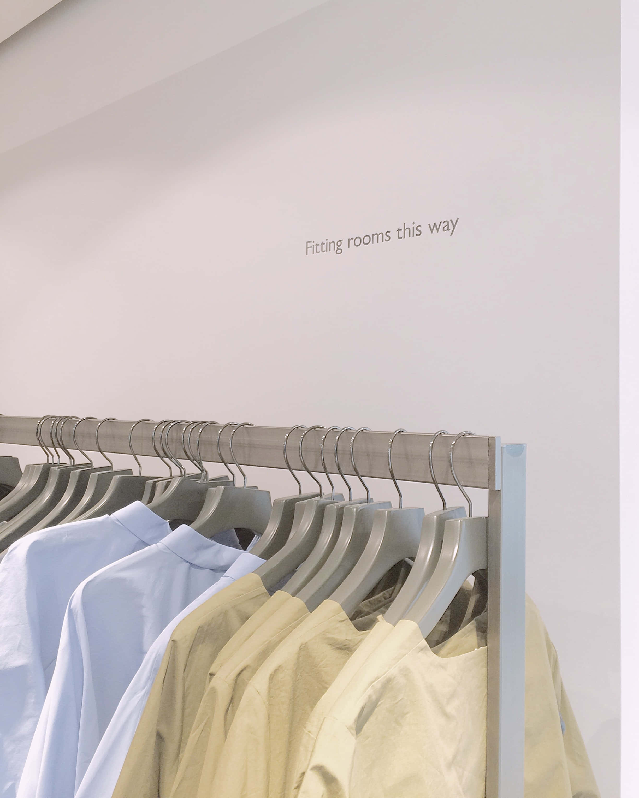 Clothes 桌布 壁紙 — 簡約衣架，掛有淺藍色和米色襯衫，柔和室內燈光下，牆上文字指引到試衣間。