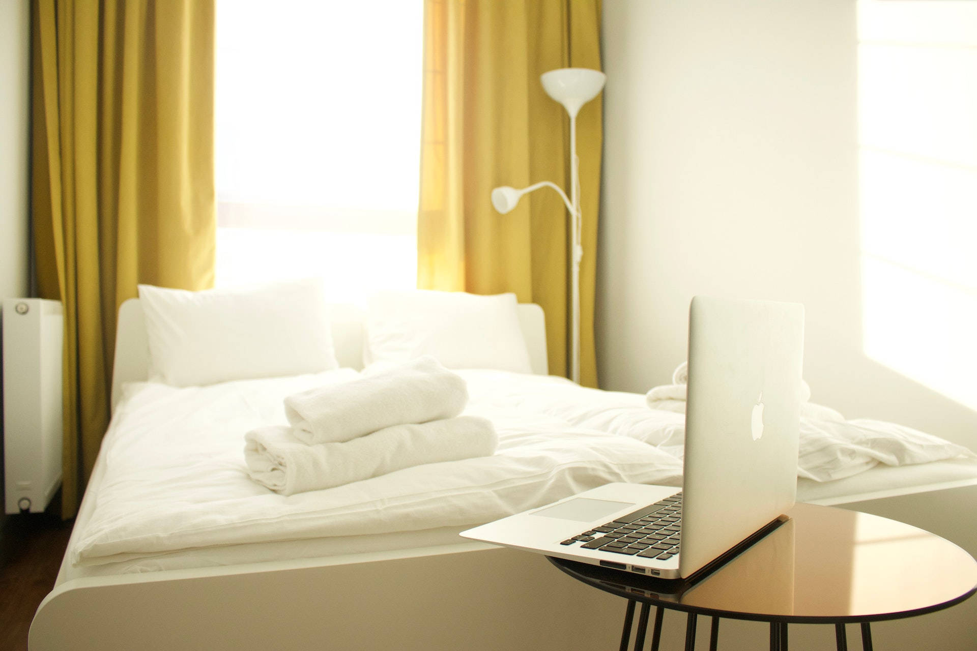bed 桌布 壁紙 — 簡約風格的臥室，白色床單和金色窗簾沐浴在柔和晨光中，床頭櫃上放著一部筆記型電腦。